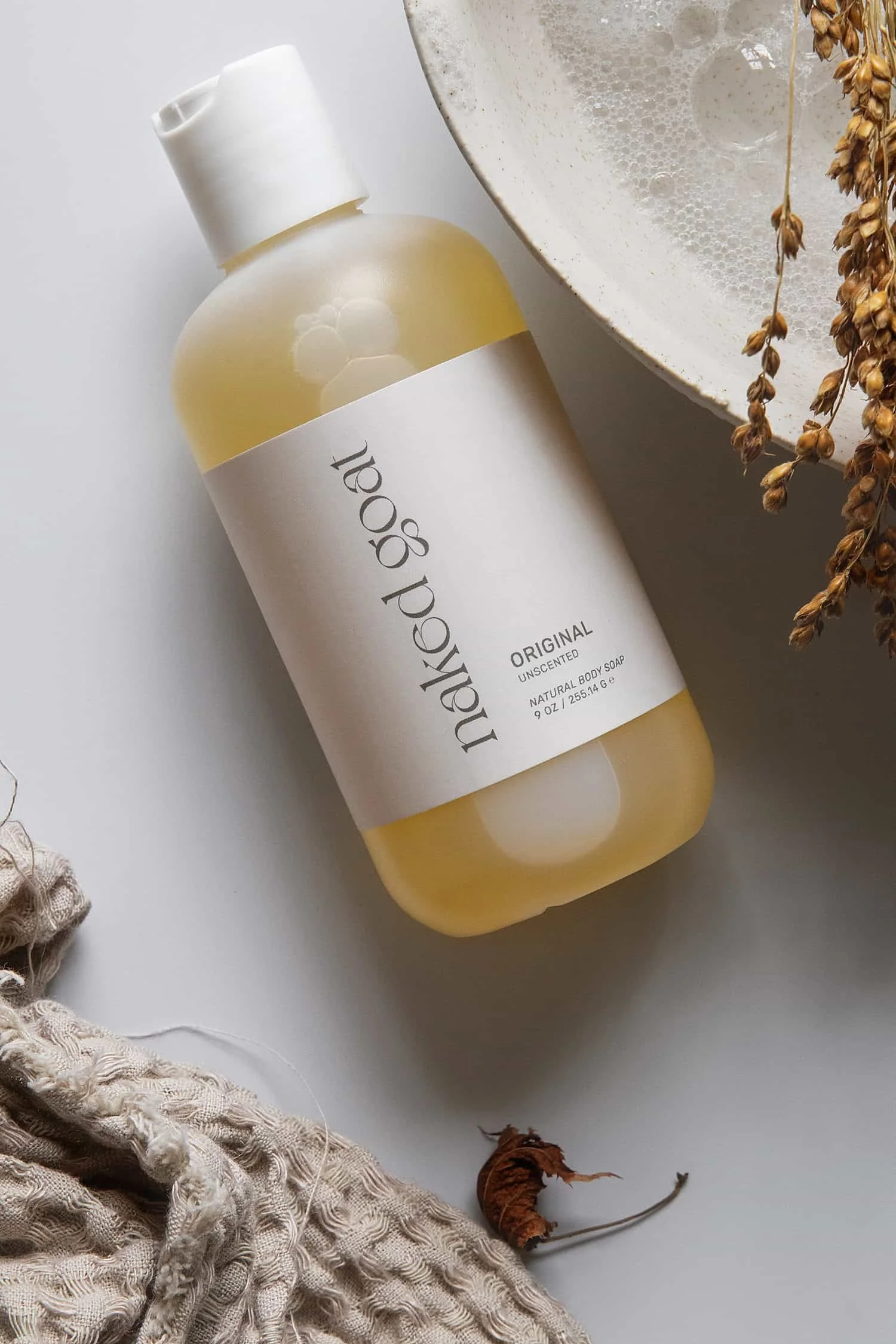 Flat lay showing Naked Goat bubble bath next to a towel and rustic bowl