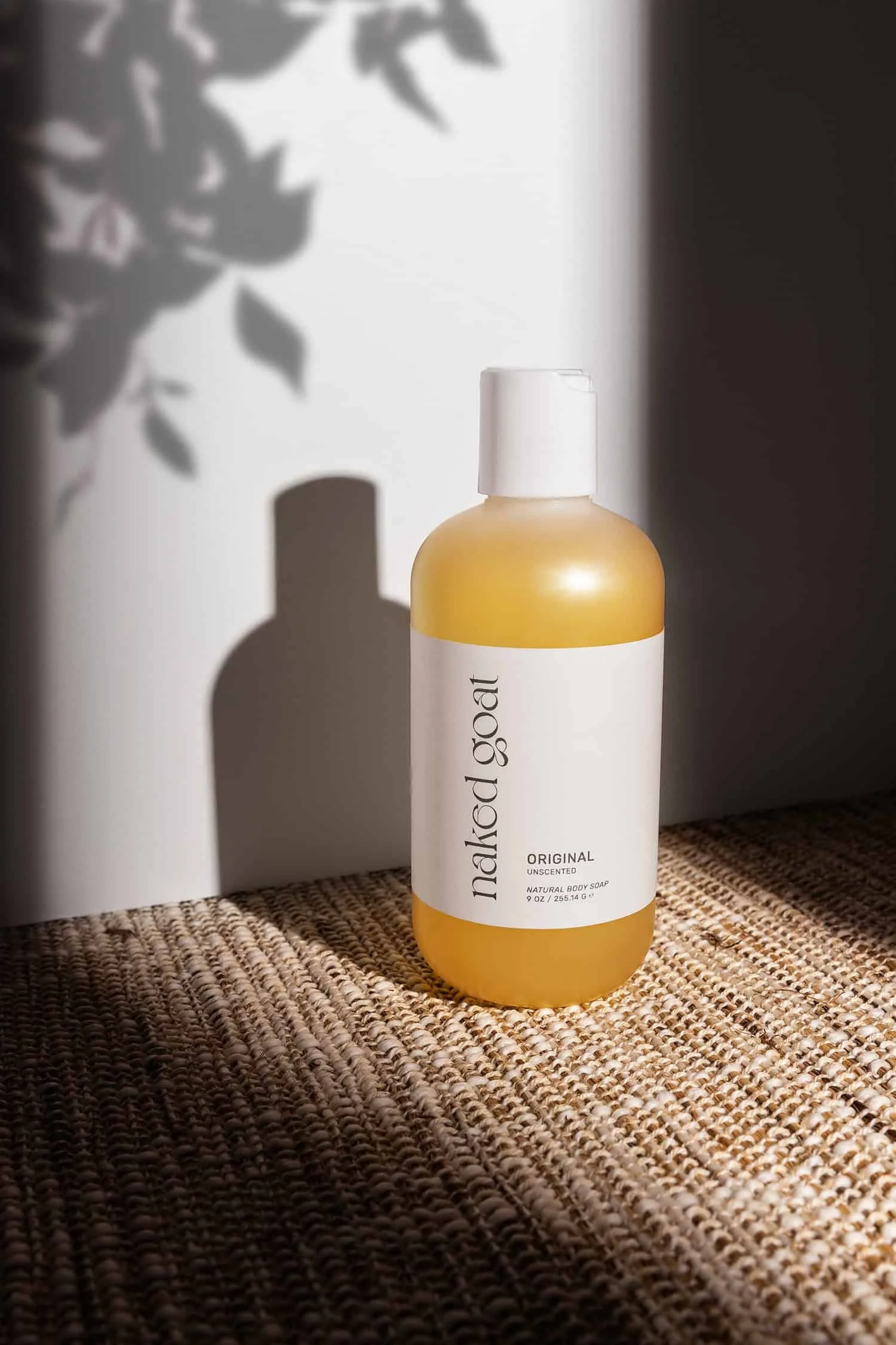 Bottle of Naked Goat bubble bath in a ray of sunlight with leafy shadows behind it