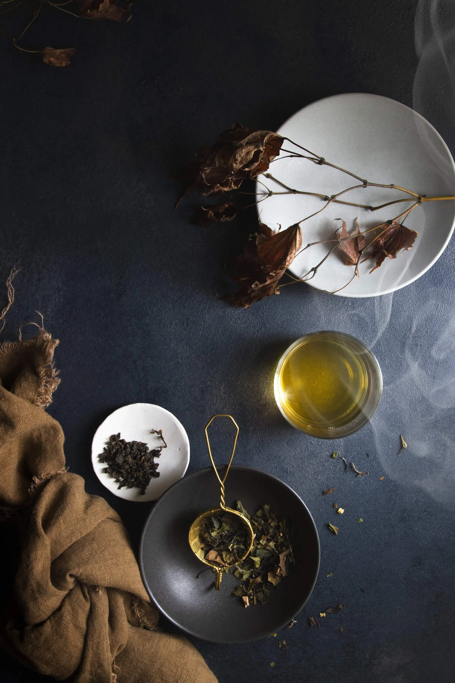 Moody flat lay showing a cup of steaming tea next to several bowls of loose tea