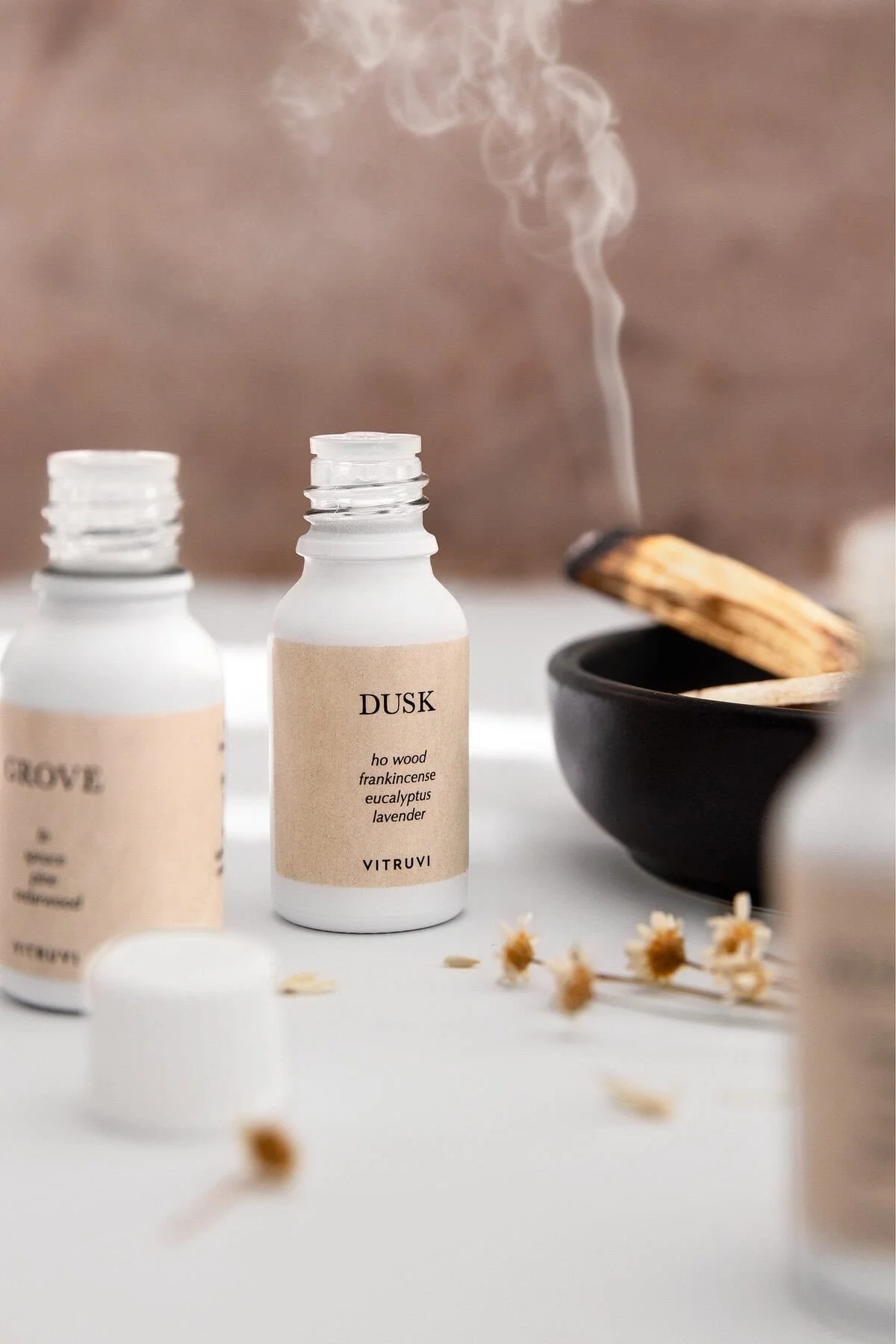 Picture of two Vitruvi essential oil bottles next to a bowl of smoking Palo Santo