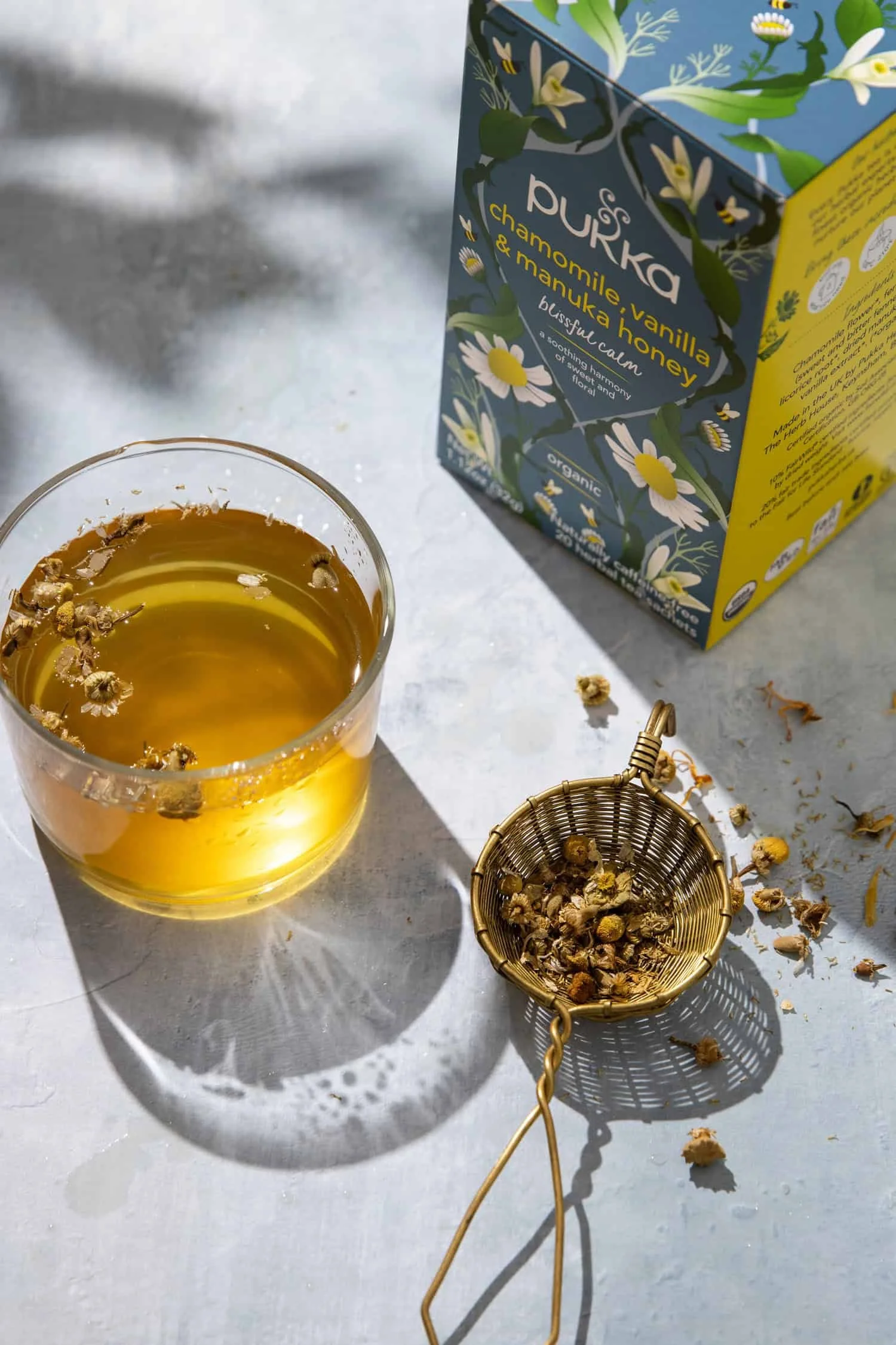 A cup of chamomile tea with flower blossoms and a box of Pukka tea behind it