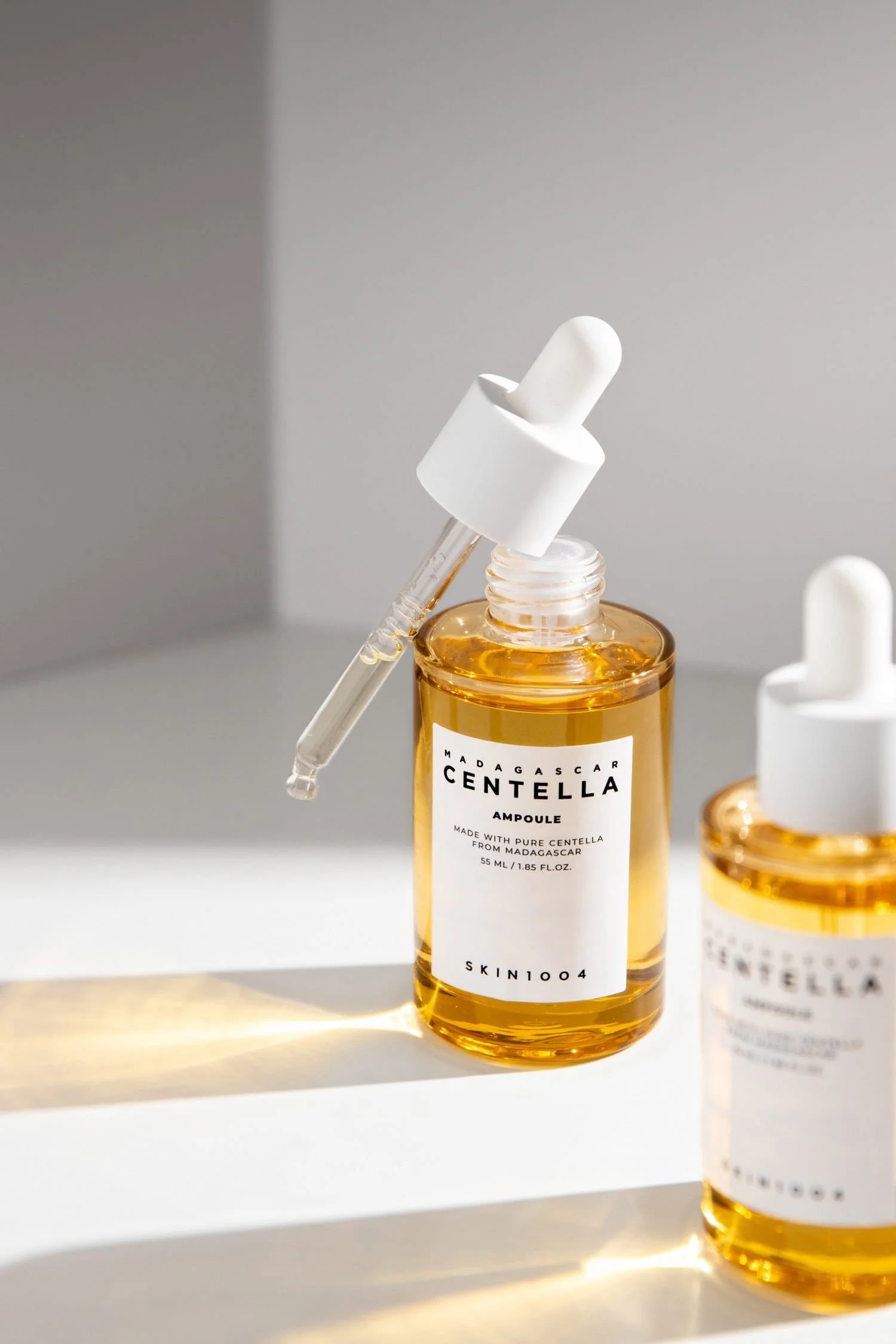 Two Centella serum bottles with light shining through in front of a white background