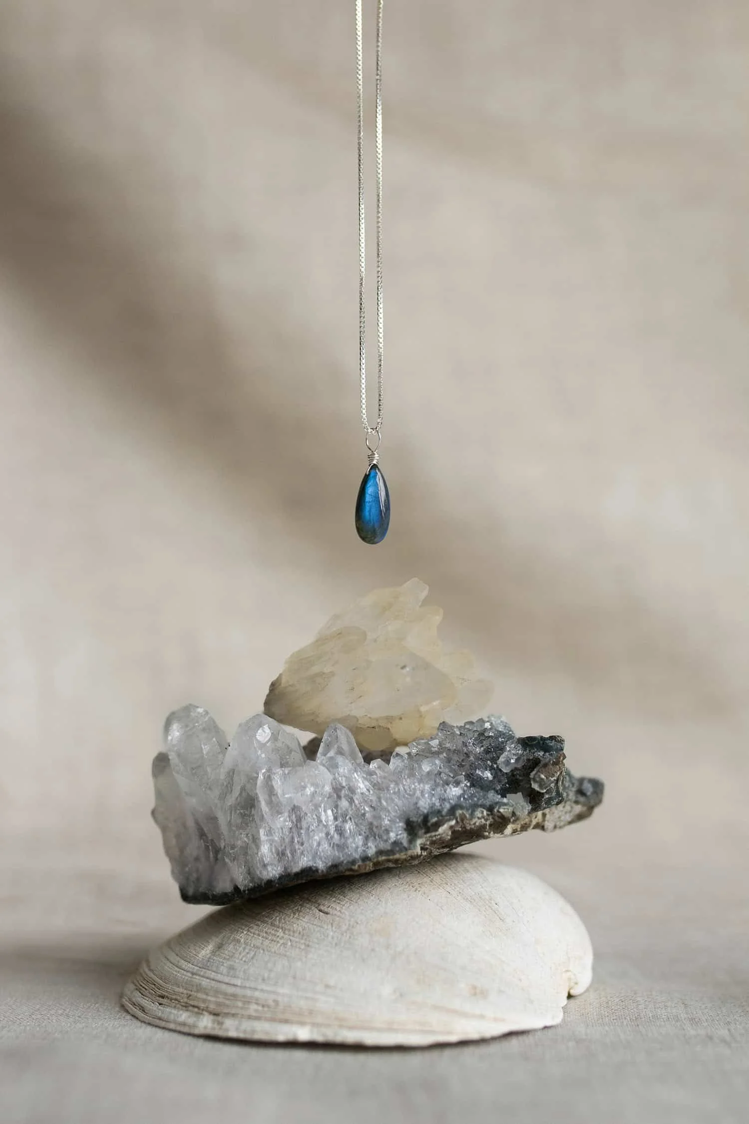 A blue labradorite crystal necklace dangling over a stacked gemstones