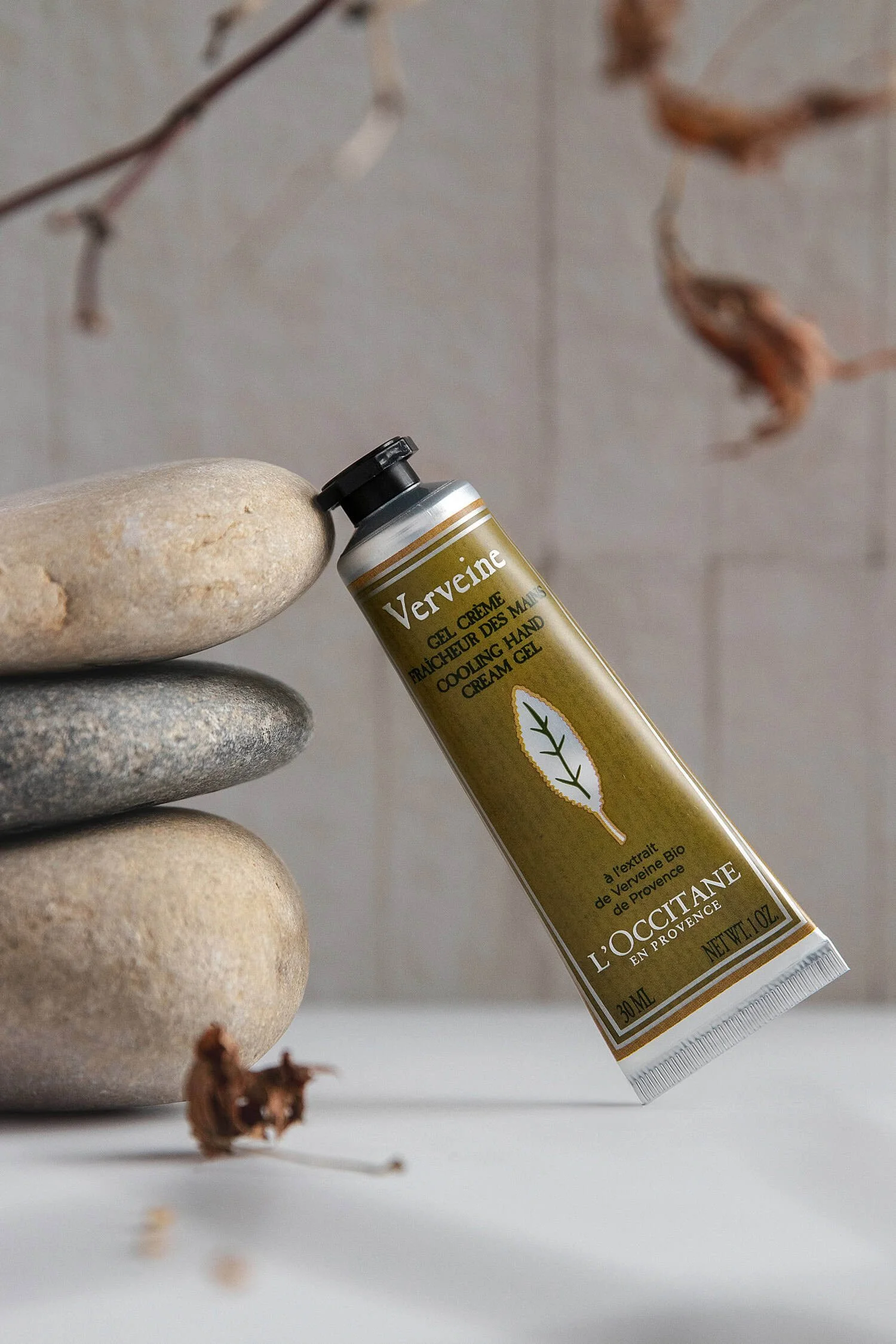 L'occitane lotion styled next to a stack of stones with dried leaves in the background
