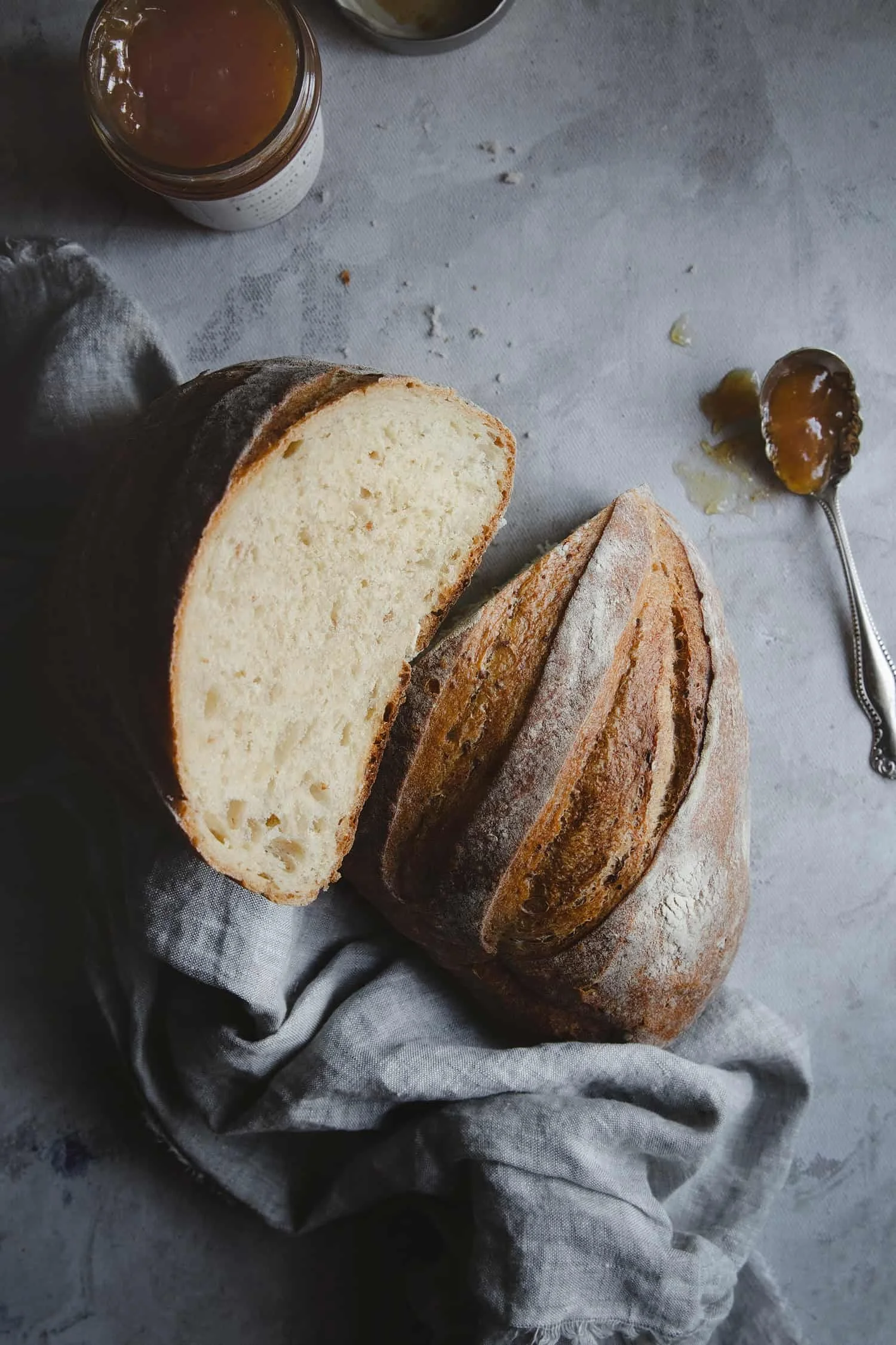 Loaf of fresh baked bread sliced in half next to a jar of apricot jam