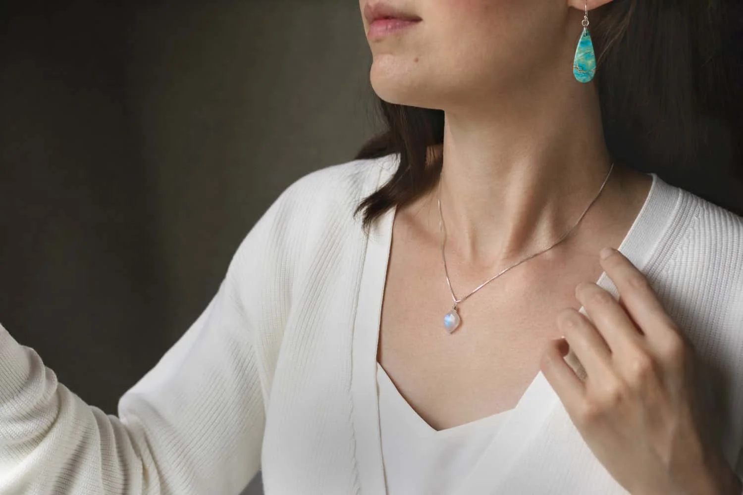 A woman wearing a gemstone necklace and earrings looking out a window