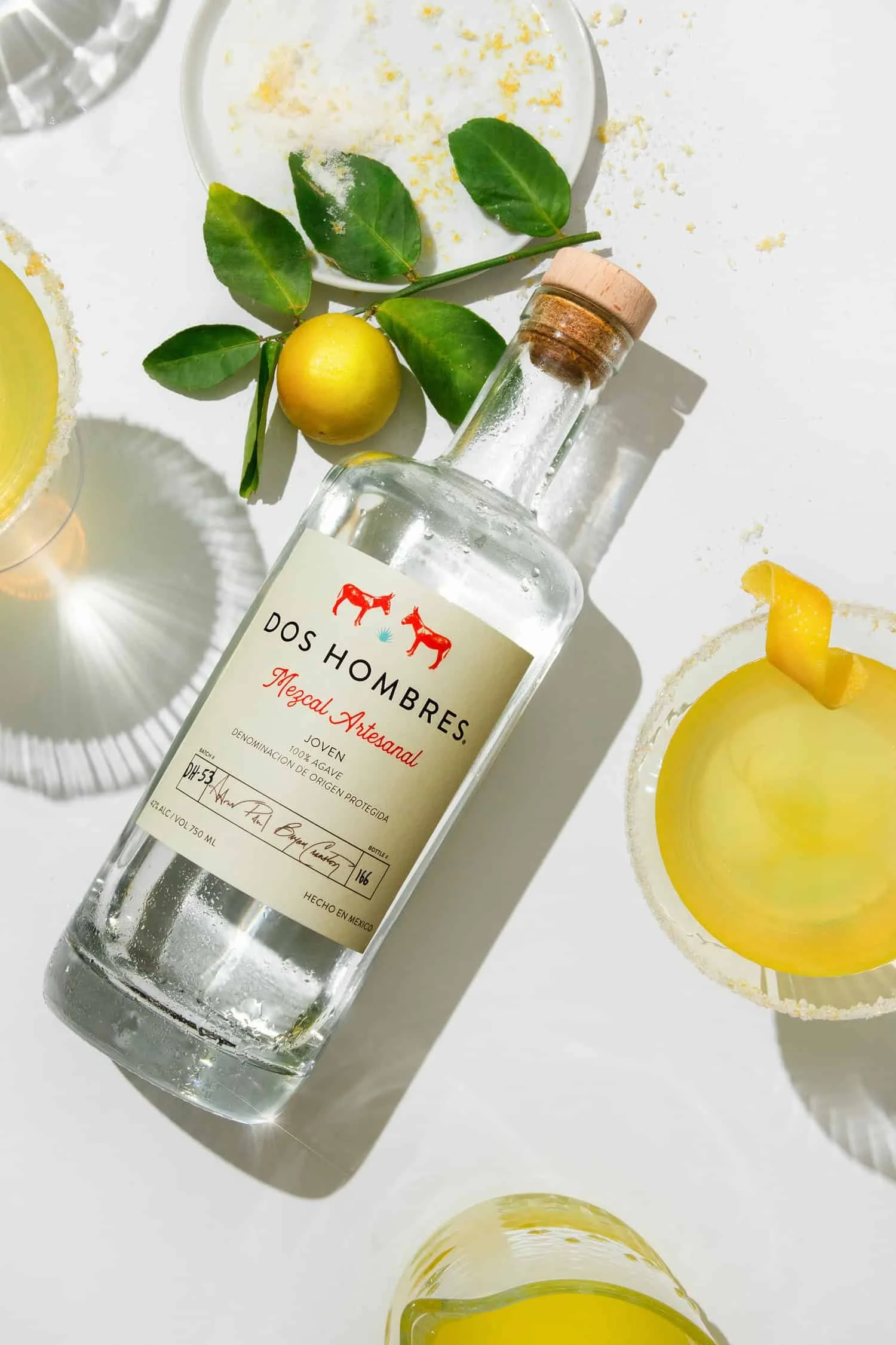 Dos Hombres mezcal bottle surrounded by fresh lemons and several cocktails