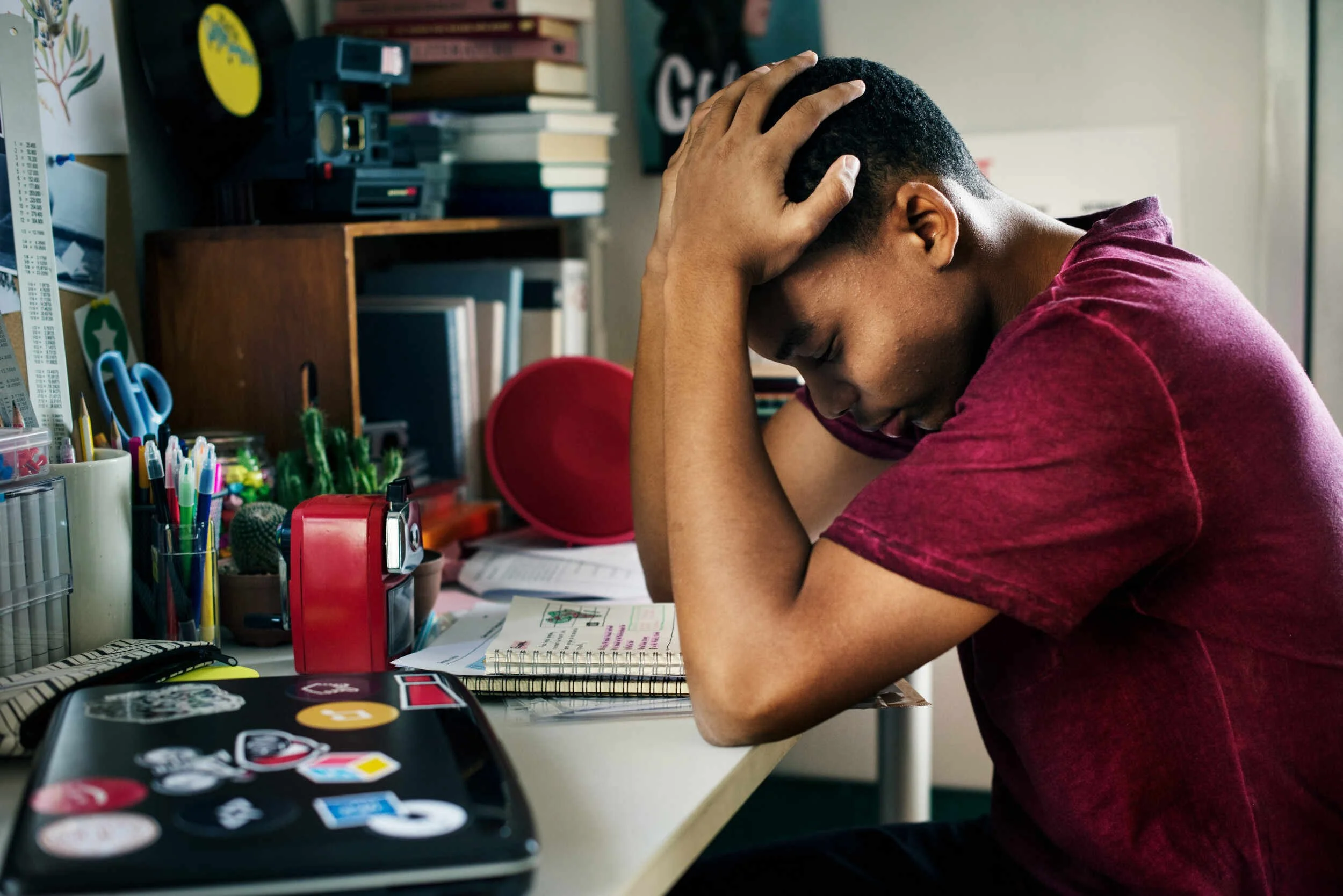 A young man tired with both hands on his head sitting at his desk - how to get out of a rut