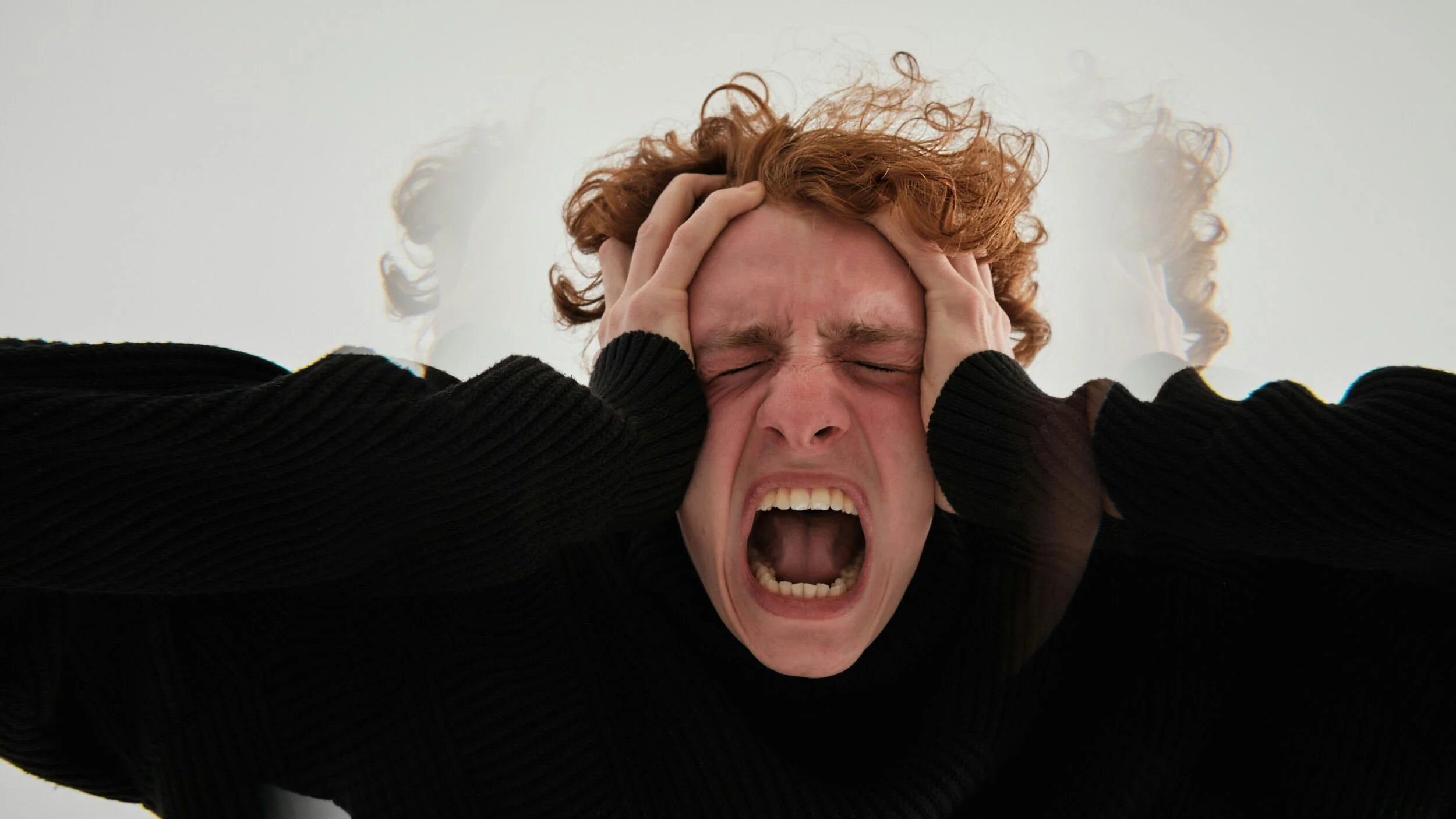 A man with red hair holding both hands to his head and screaming - successful but unfulfilled