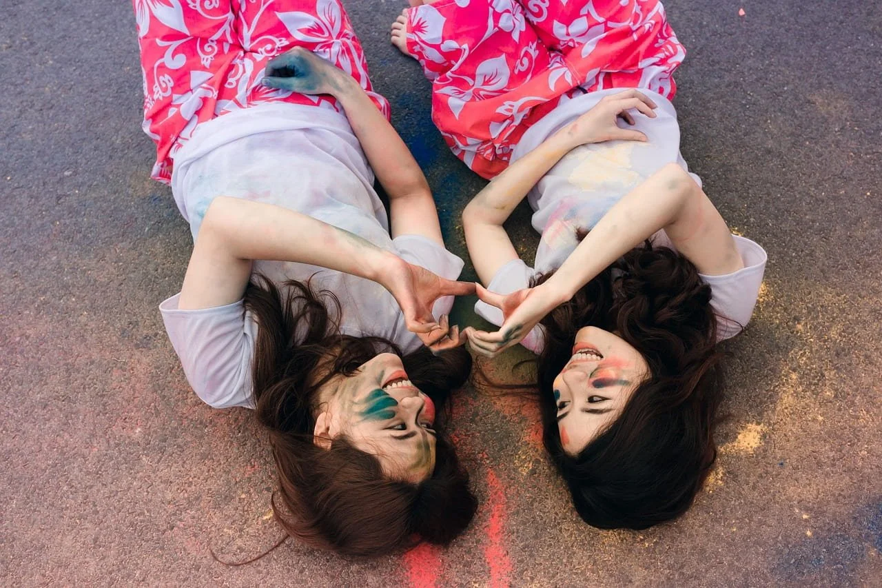 two women laying on their backs on the ground holding hands in a heart shape - burnout recovery phoenix