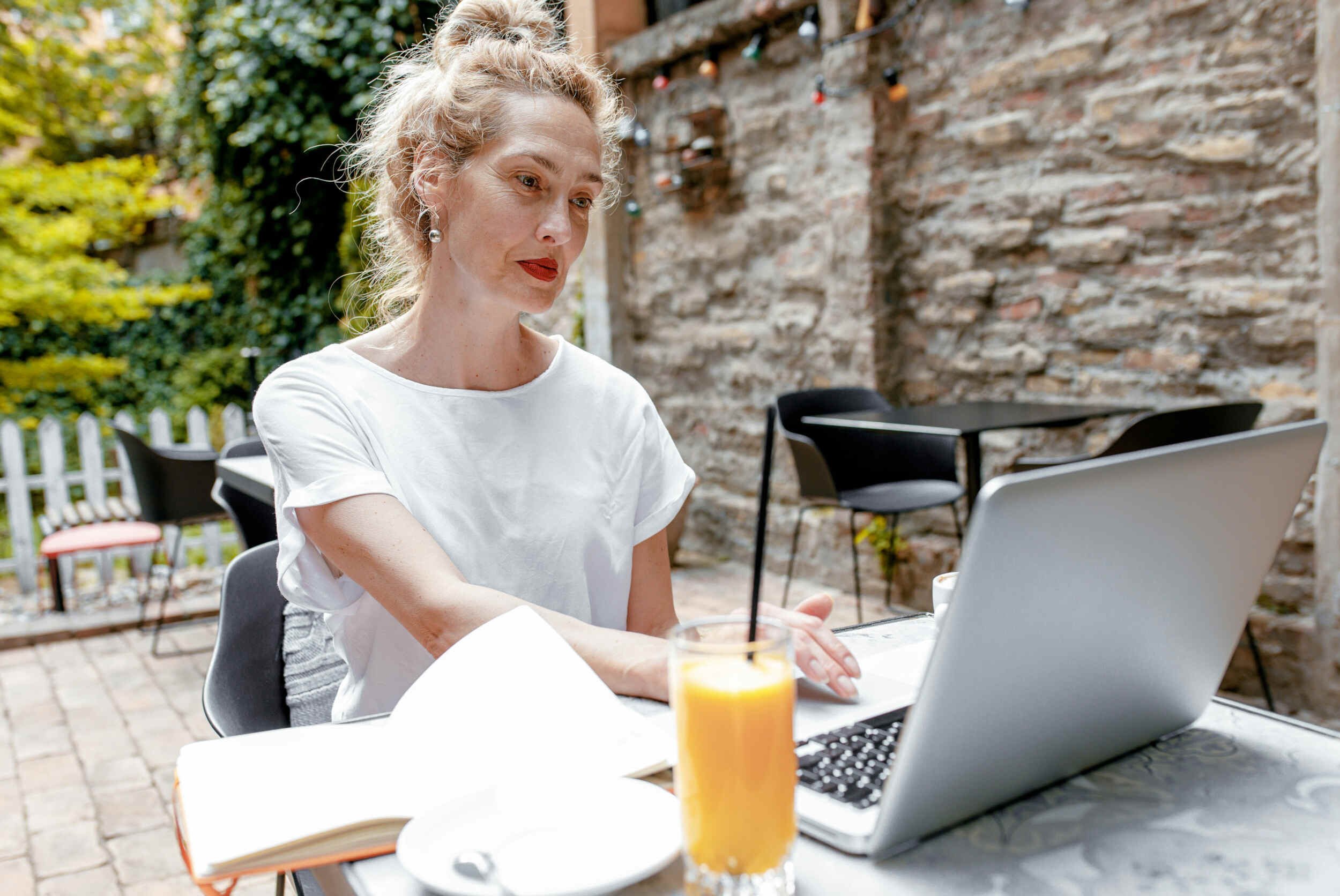 A women outside in front of her laptop with orange juice on a table - imposter syndrome at work