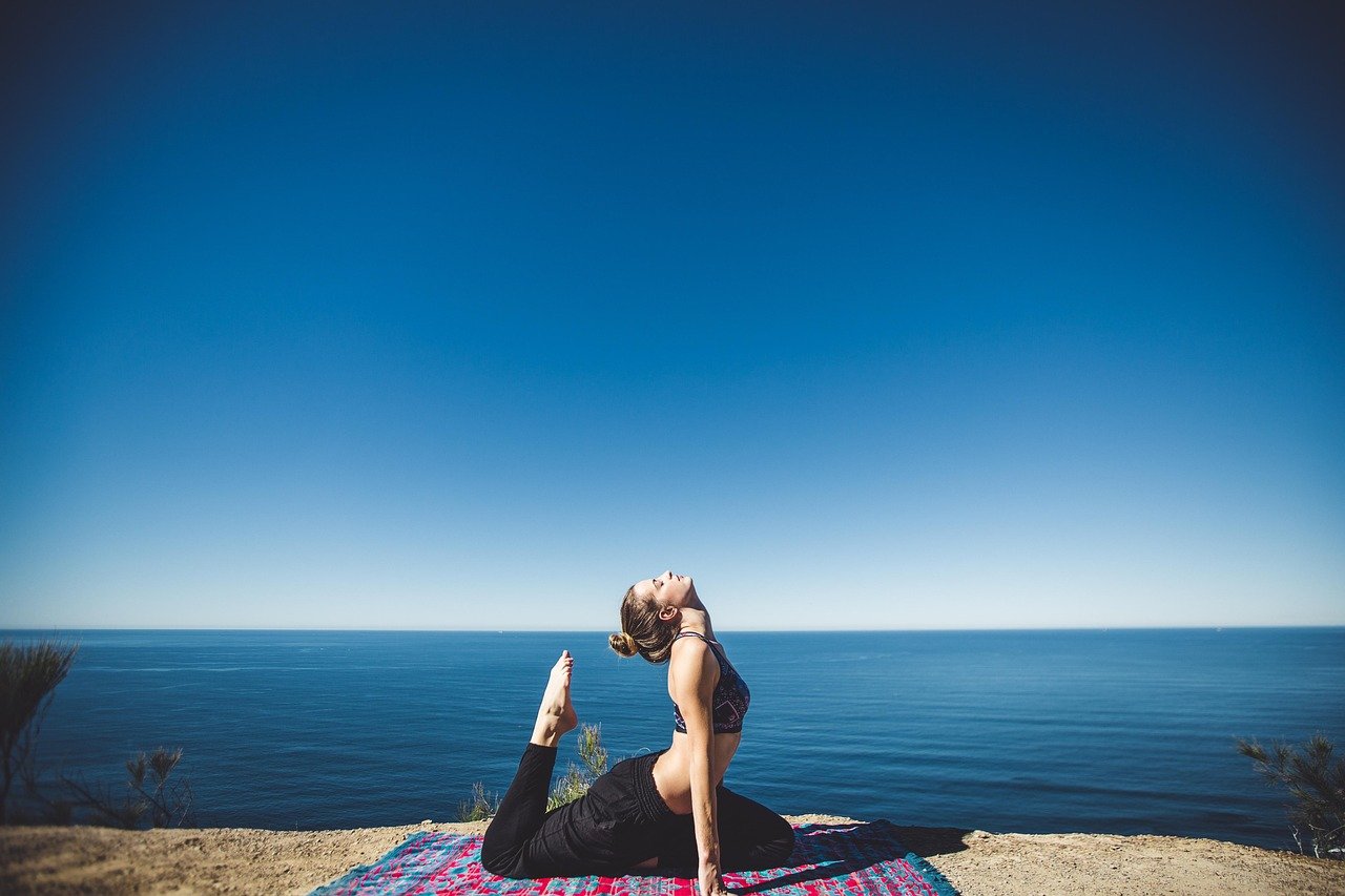 A women doing yoga on a colored mat above the ocean outside amongst the blue sky - multi-dimensional life