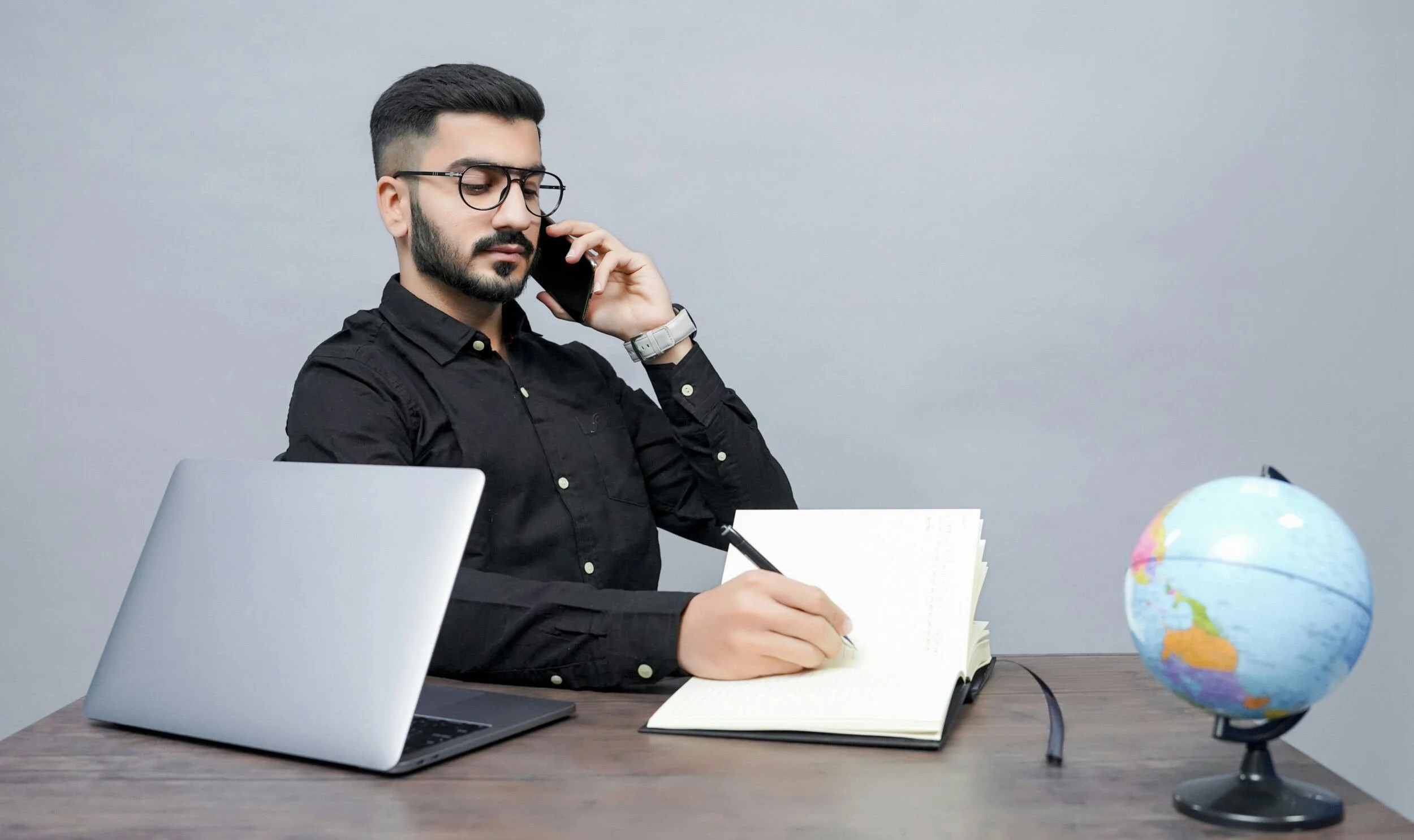 man with black shirt with phone in hand sitting at desk and taking notes - life and career coach