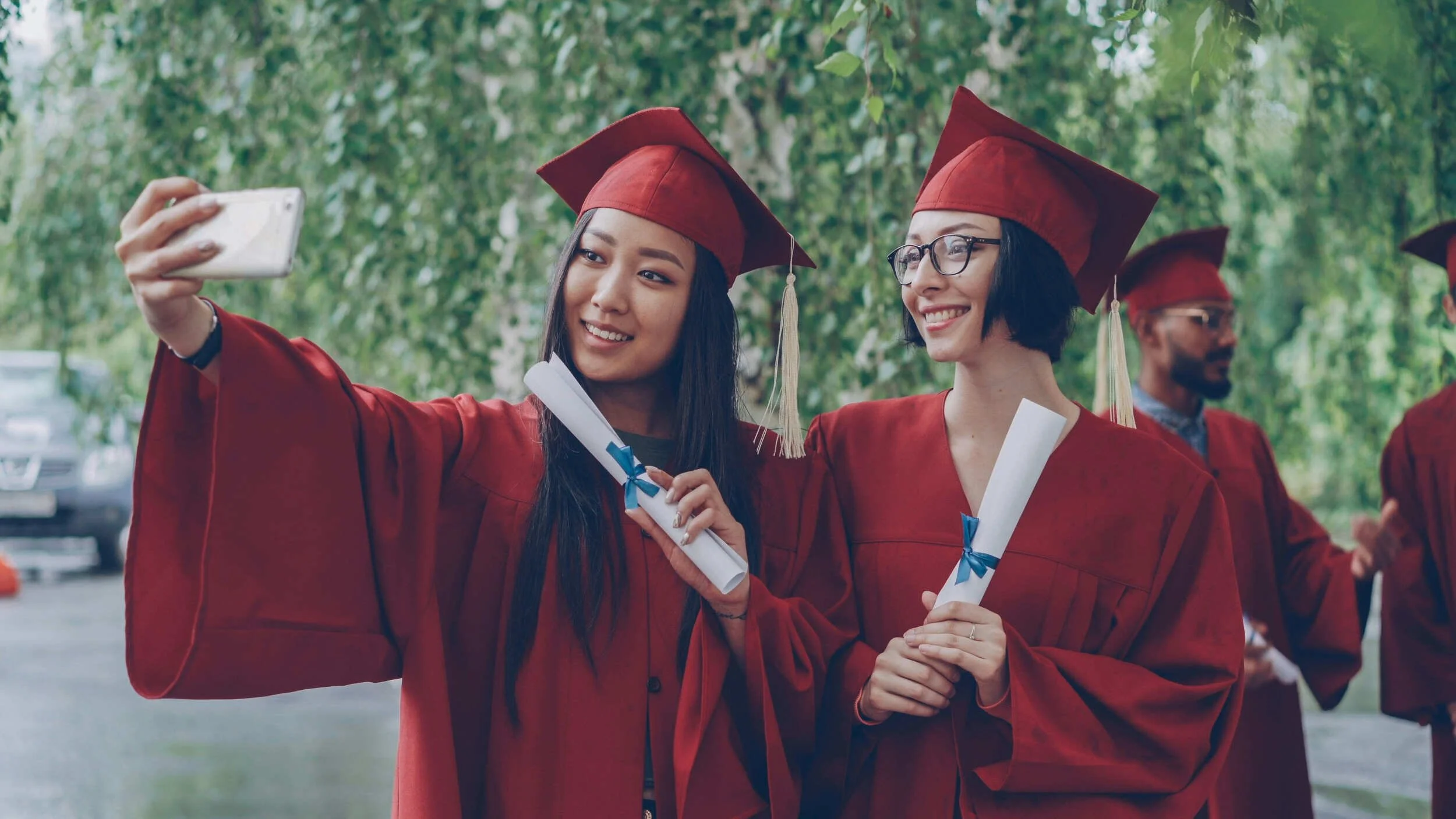 Two women wearing red graduation outfits taking a selfie picture outside - career transition coach Scottsdale