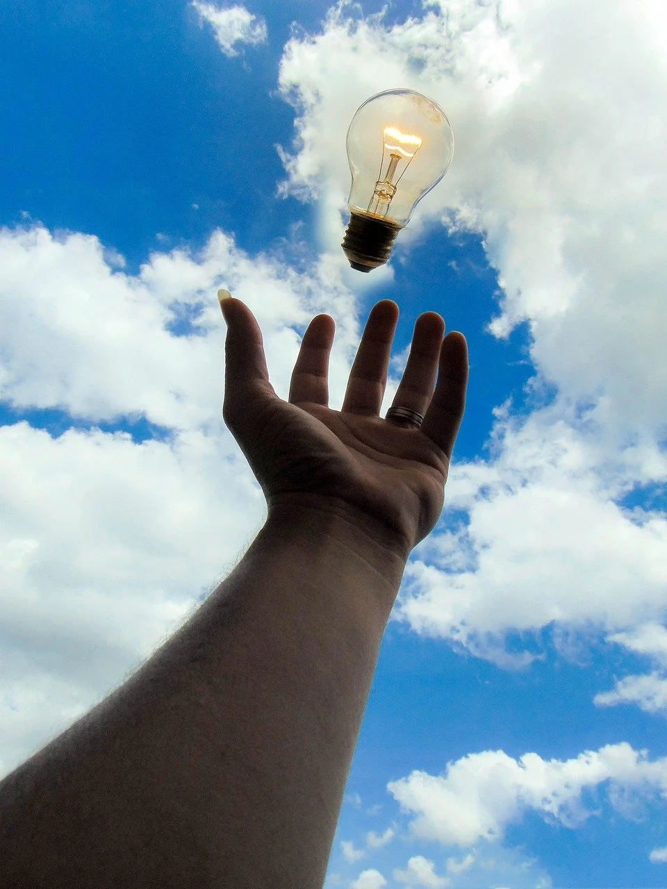 womans left hand in the air amongst the blue sky outside with a lightbulb - life and career coach Phoenix