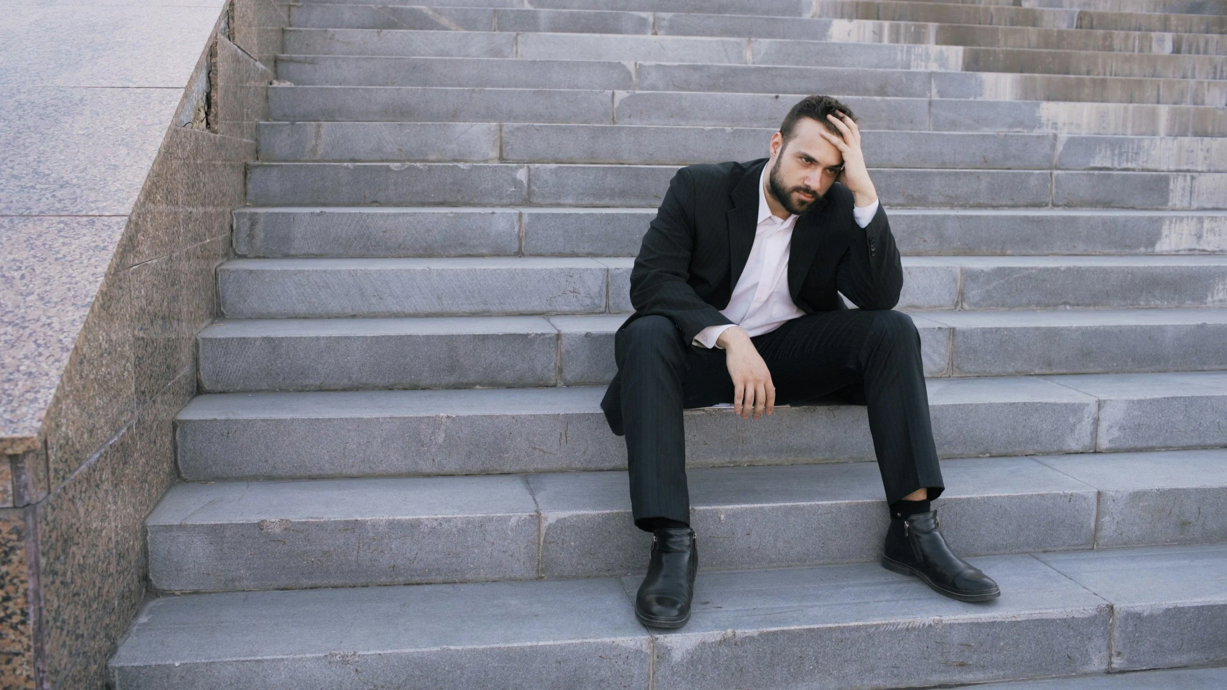 A man in a suit sitting on stairs outside sad - Career Coaching Phoenix