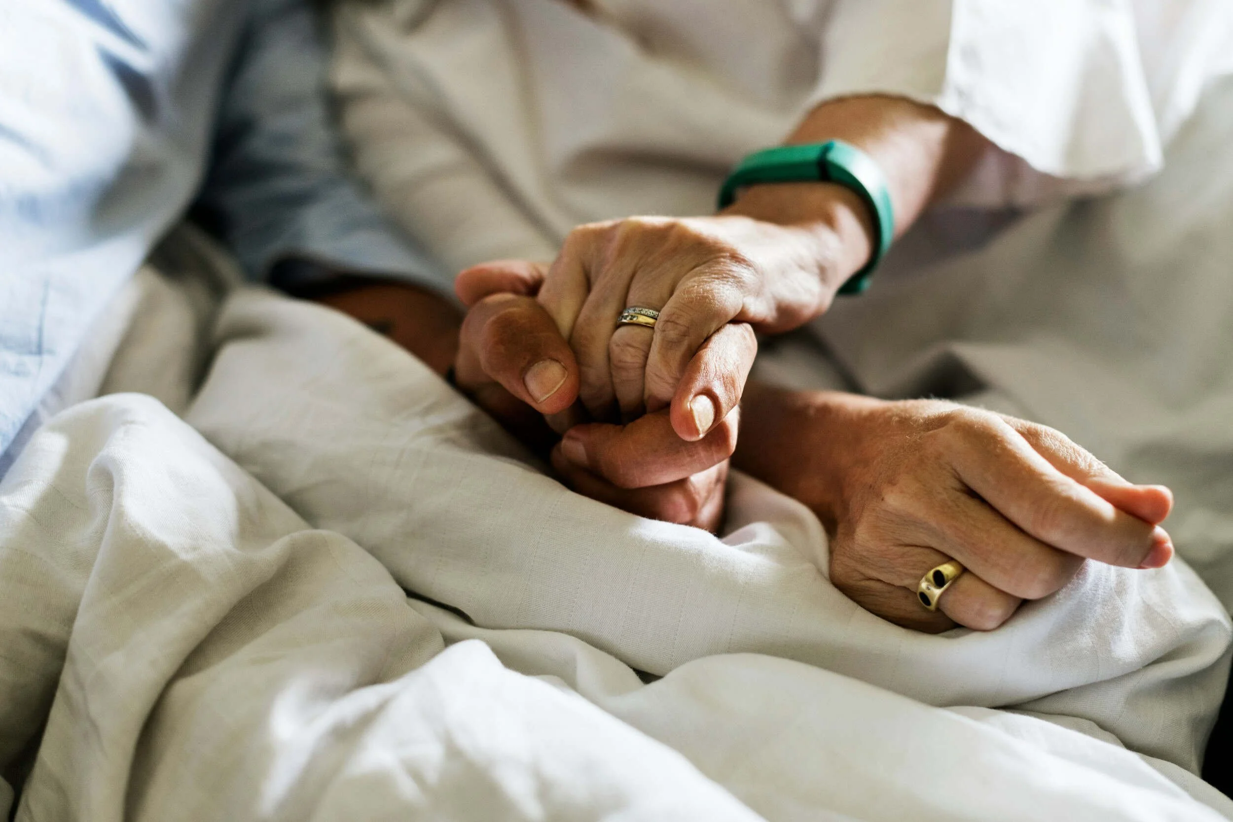 Two older hands being held in bed inside - career coach