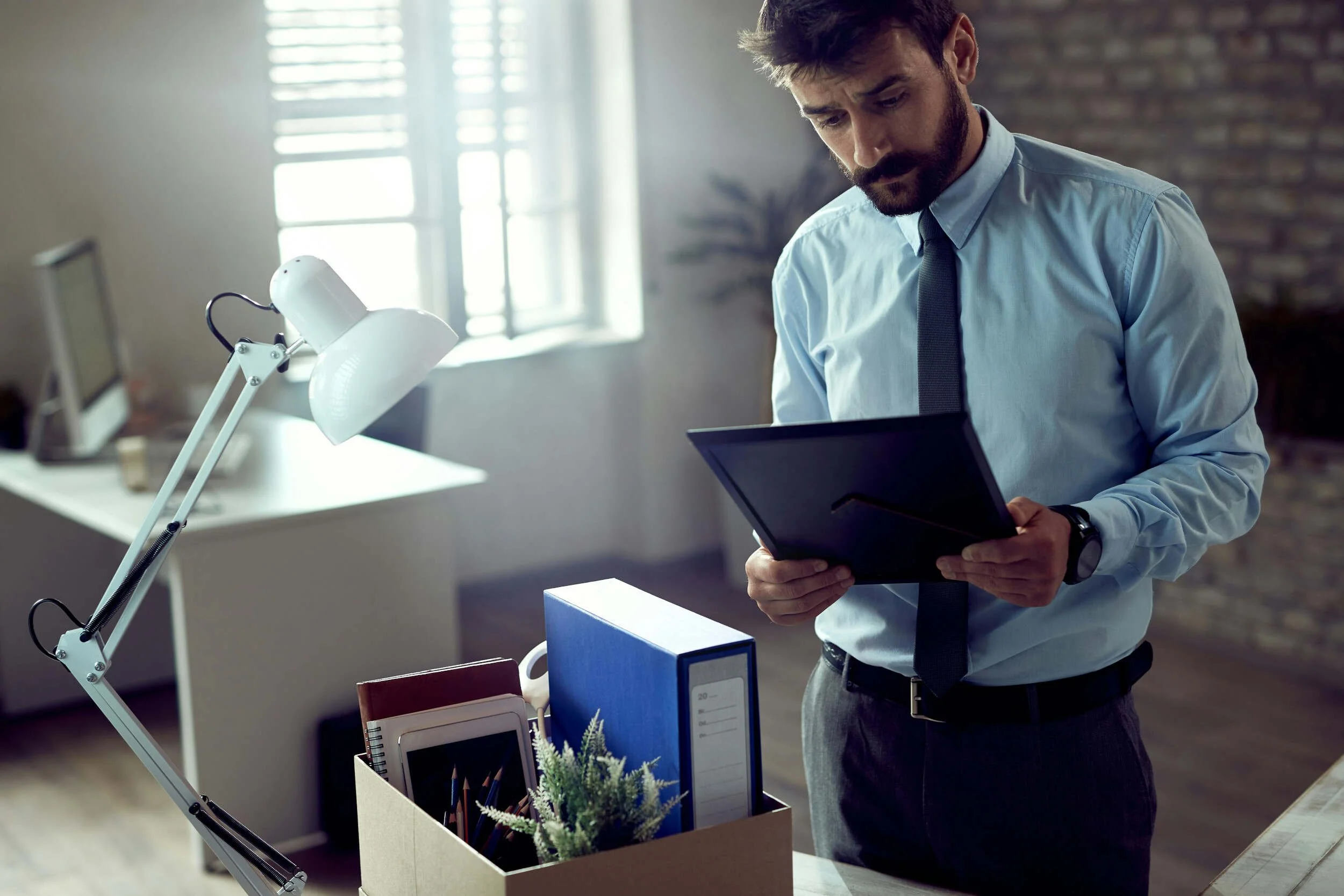 A man with a blue dress shirt on looking at a picture frame in an office - AI and the future of work