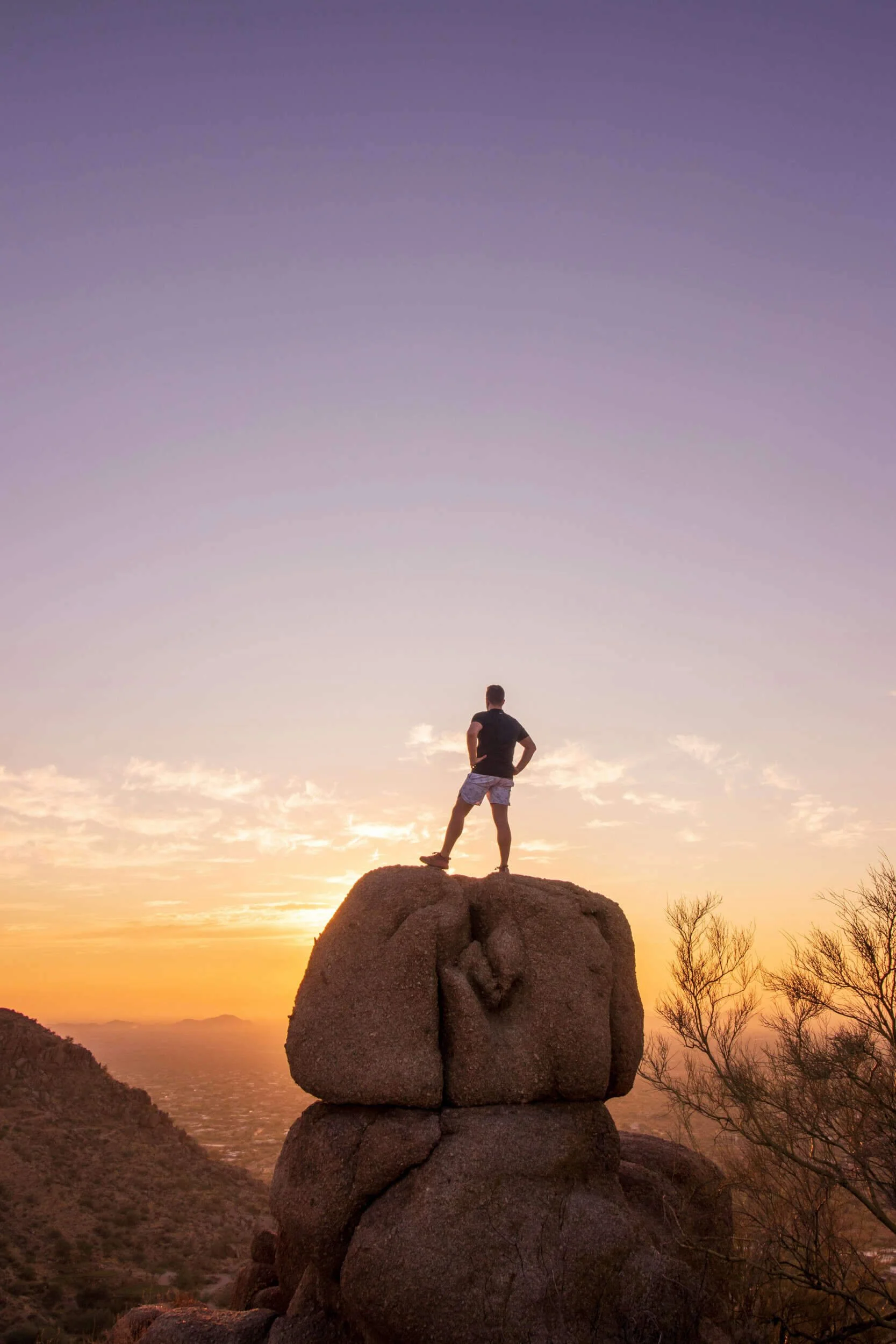 A man standing on a huge boulder outside with a sunset - life coach Scottsdale