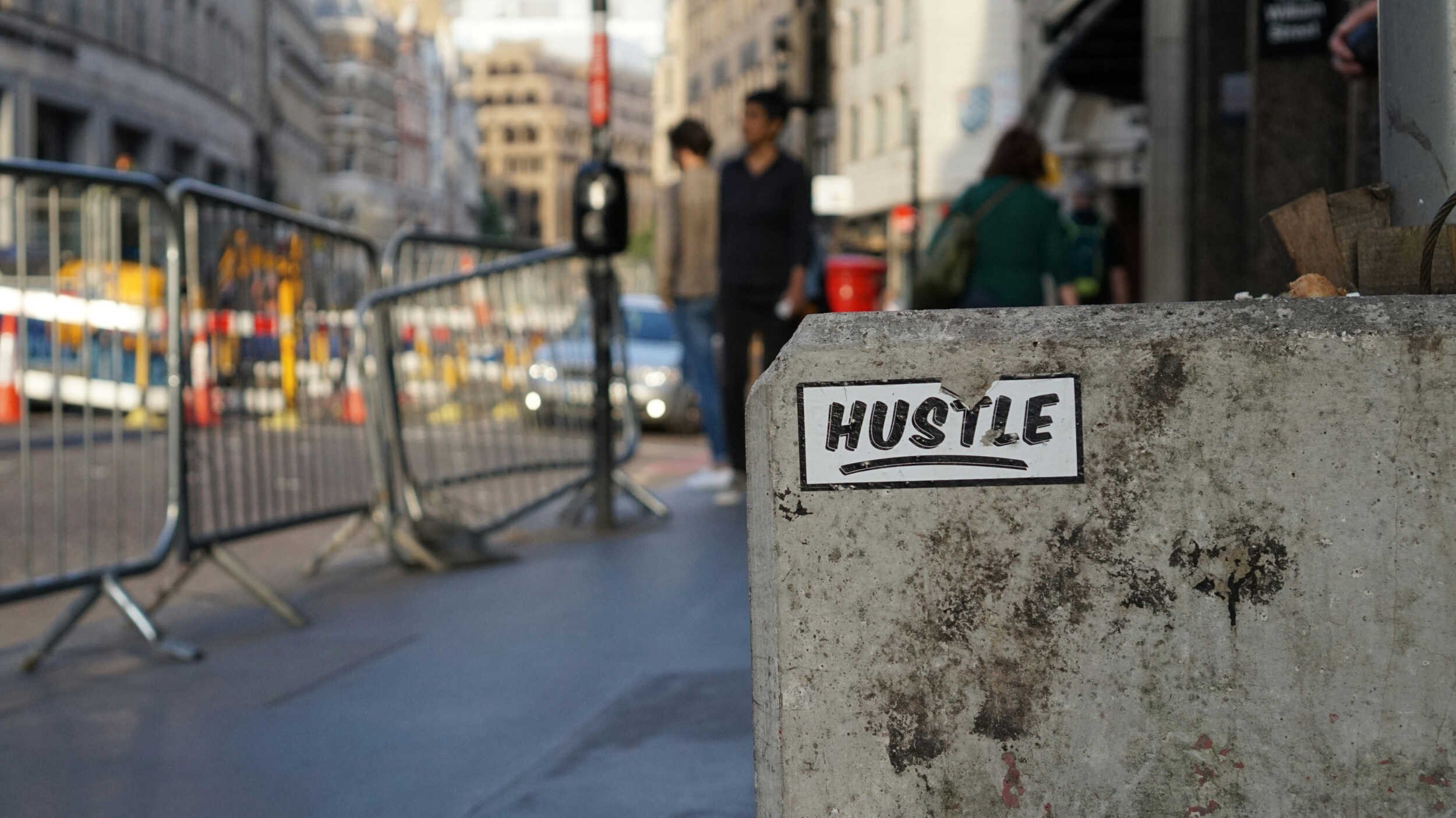 Outside in a city with a concrete slab close by with a sticker on it titled Hustle - career coach Phoenix