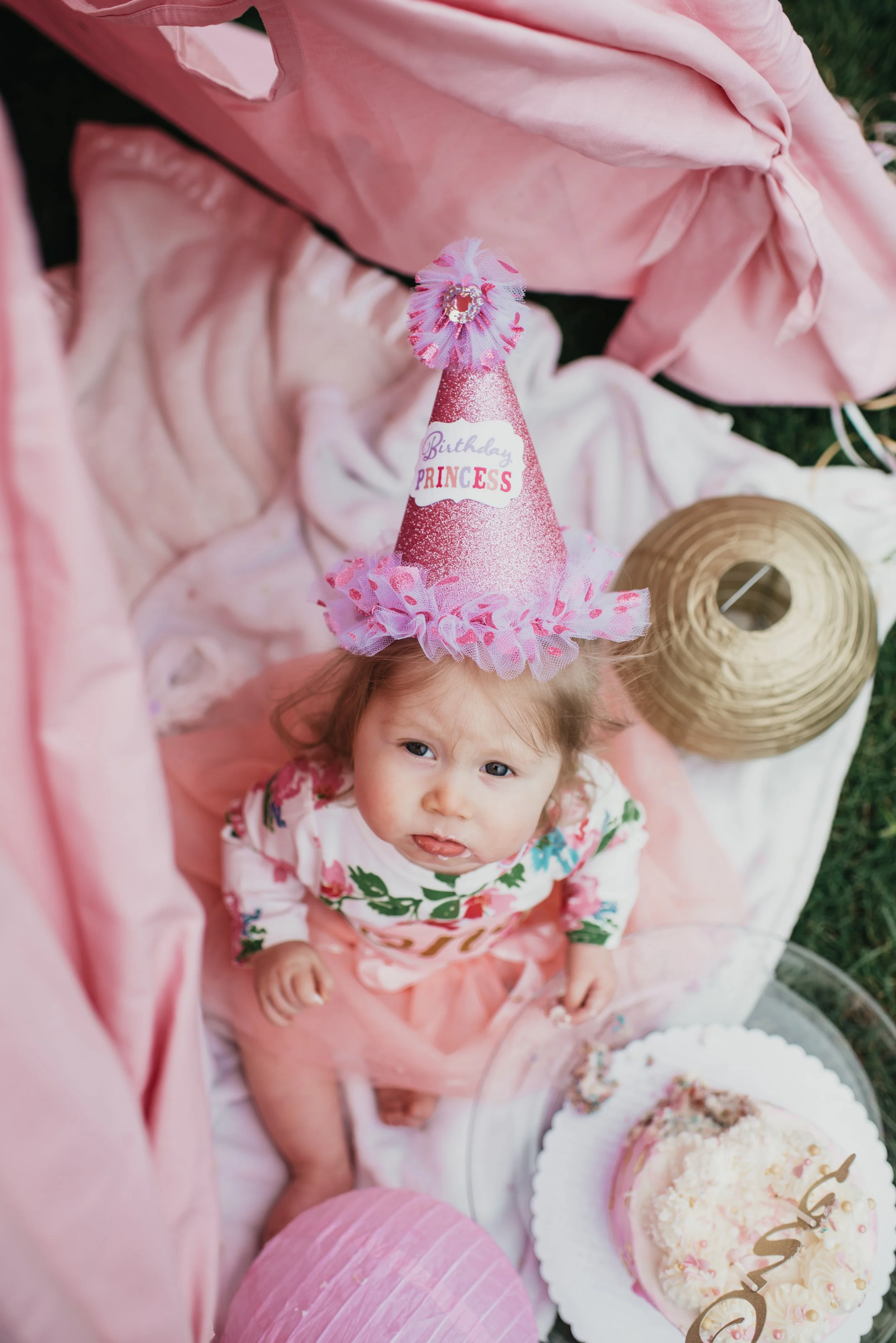 A little red haired girl looks up at the camera with a pink party hat on.