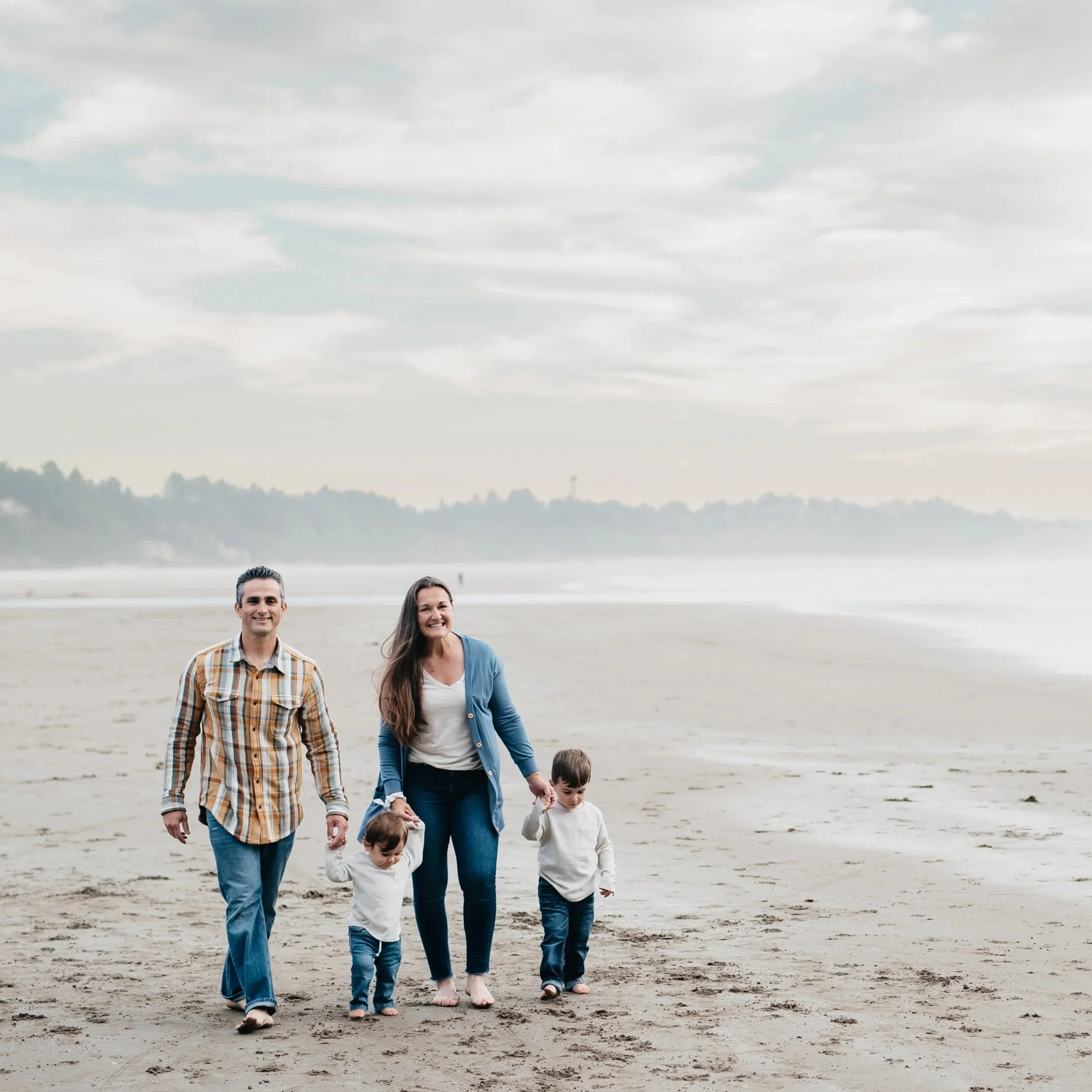 A family consisting of a mother, father, and two little boys walk along the coast.