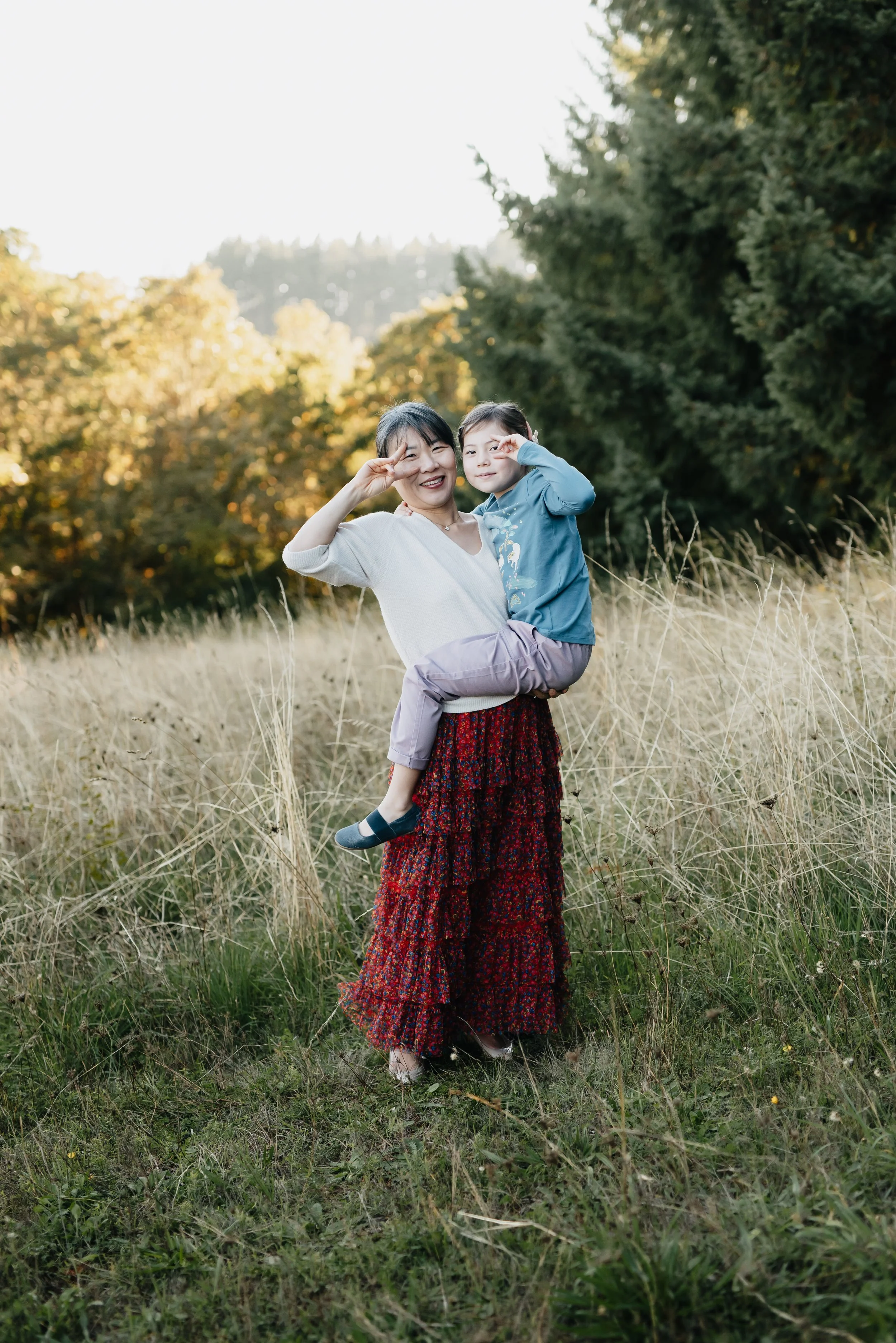 A mother and daughter of Asian descent smile and make peace signs near their eyes
