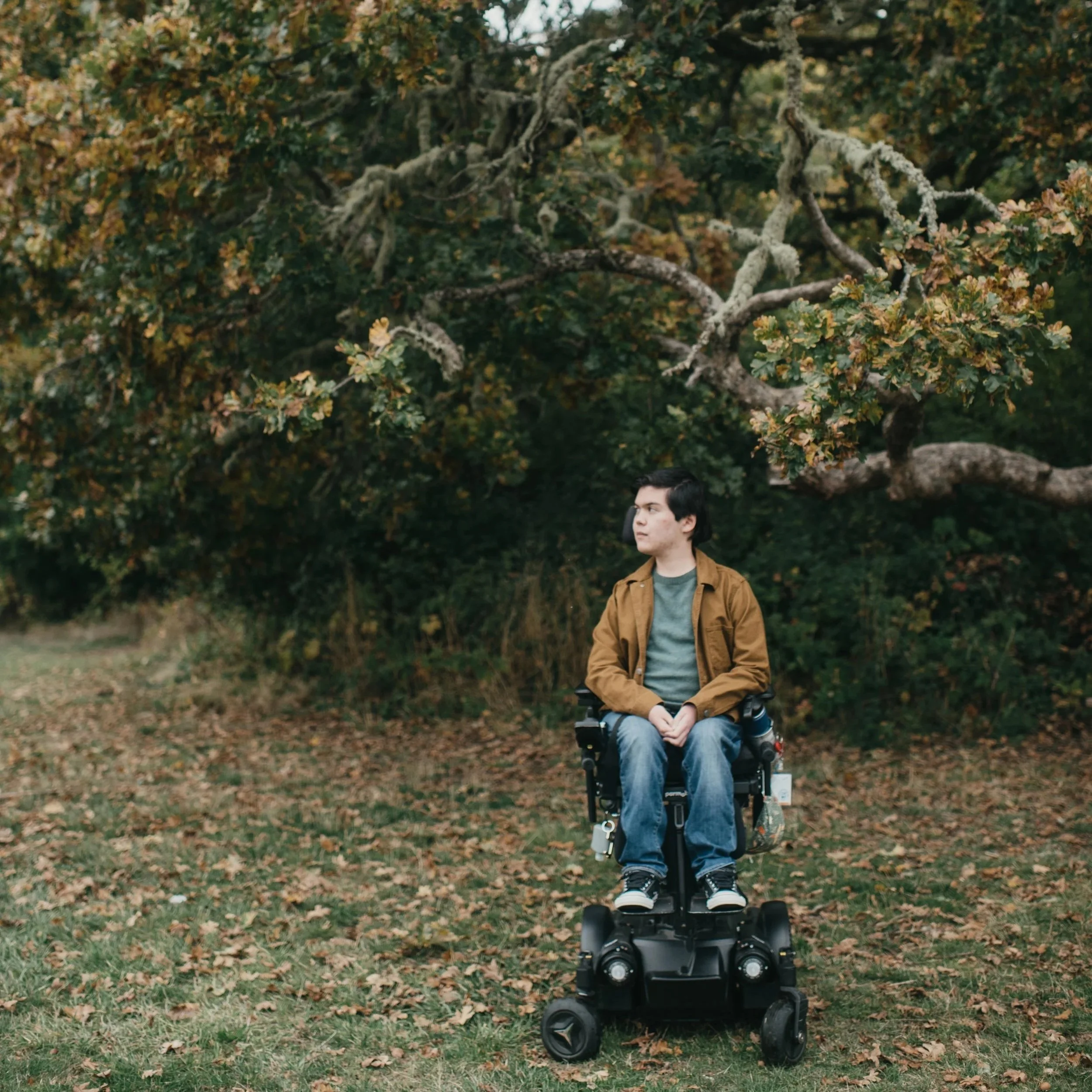 A high school senior wheelchair user looks off into the distance underneath a tree