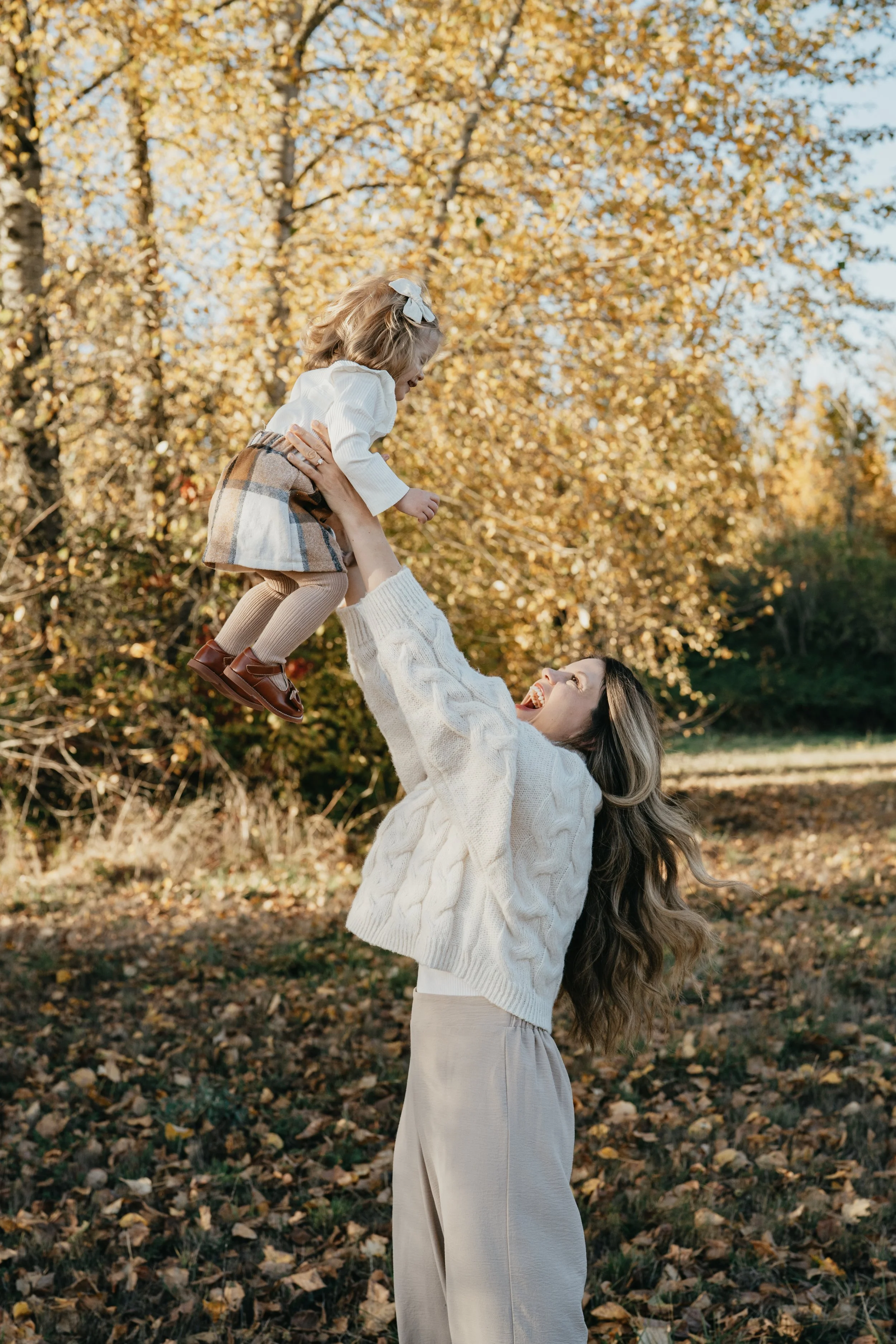 With fall leaves surrounding them, a mother holds her baby girl up in the air smiling
