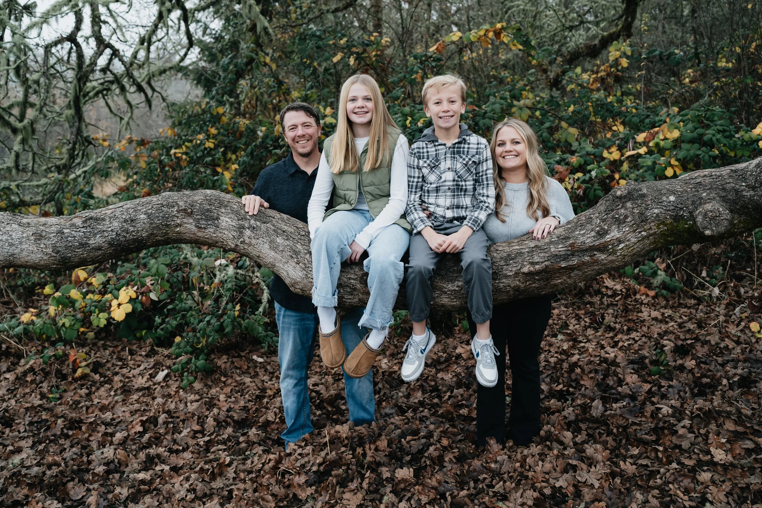 A family consisting of a mother, father, a son and a daughter are smiling at a camera next to a giant oak tree.
