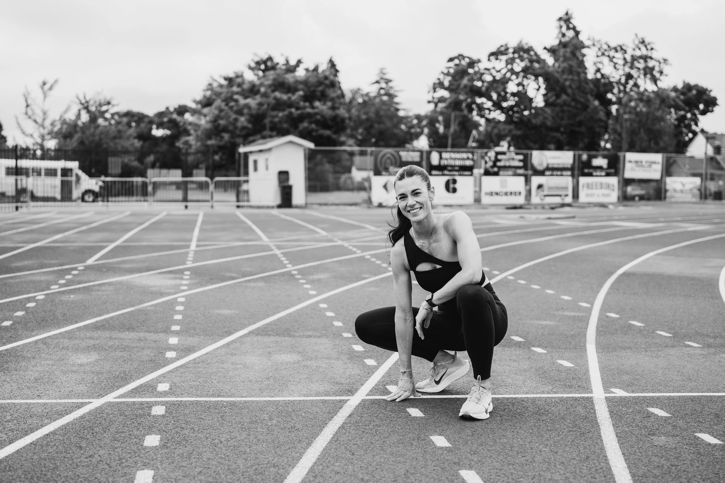An athletic female crouches on a track smiling at the camera