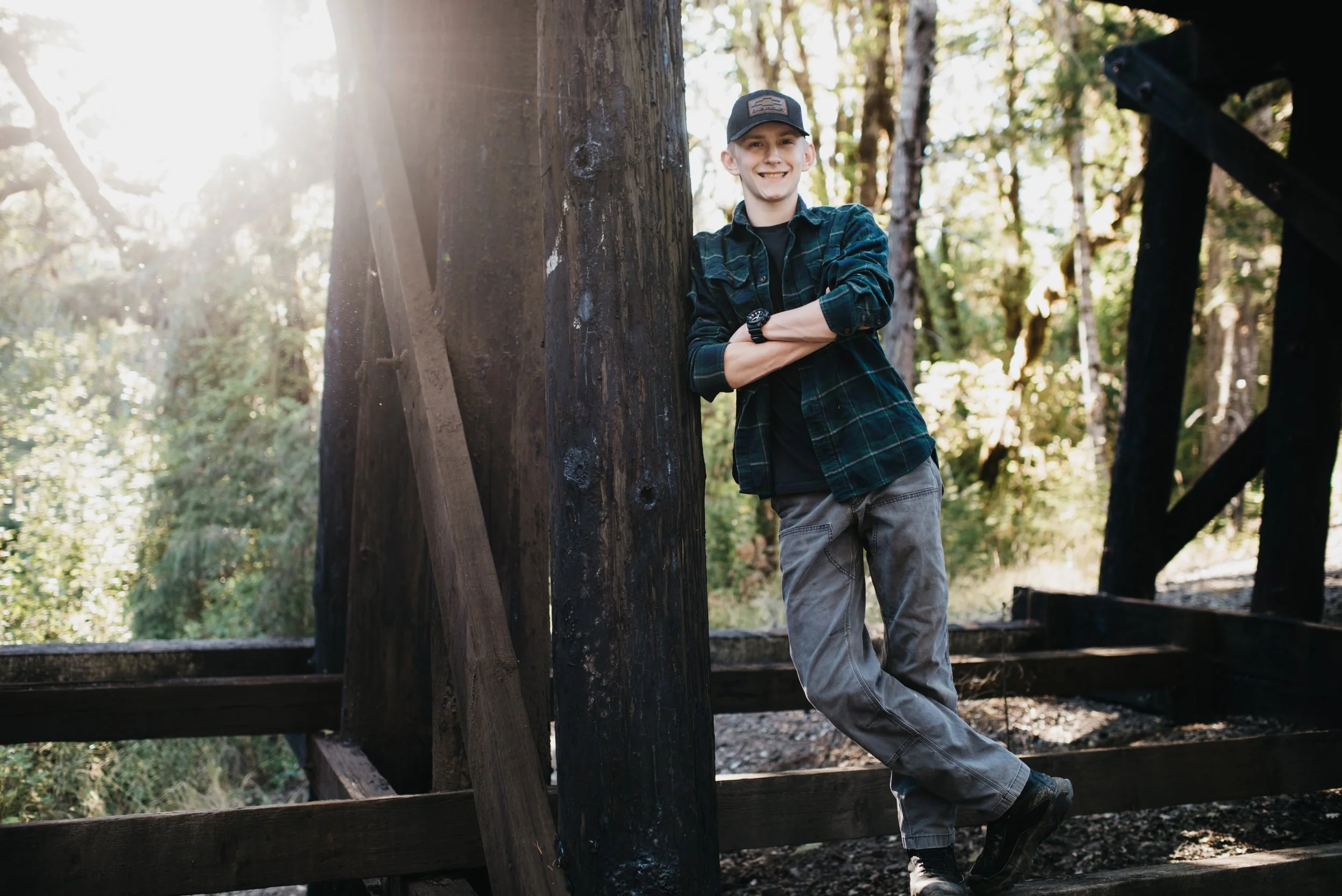 A male high school senior leans up against train tracks with a sun flare to the left of the image.