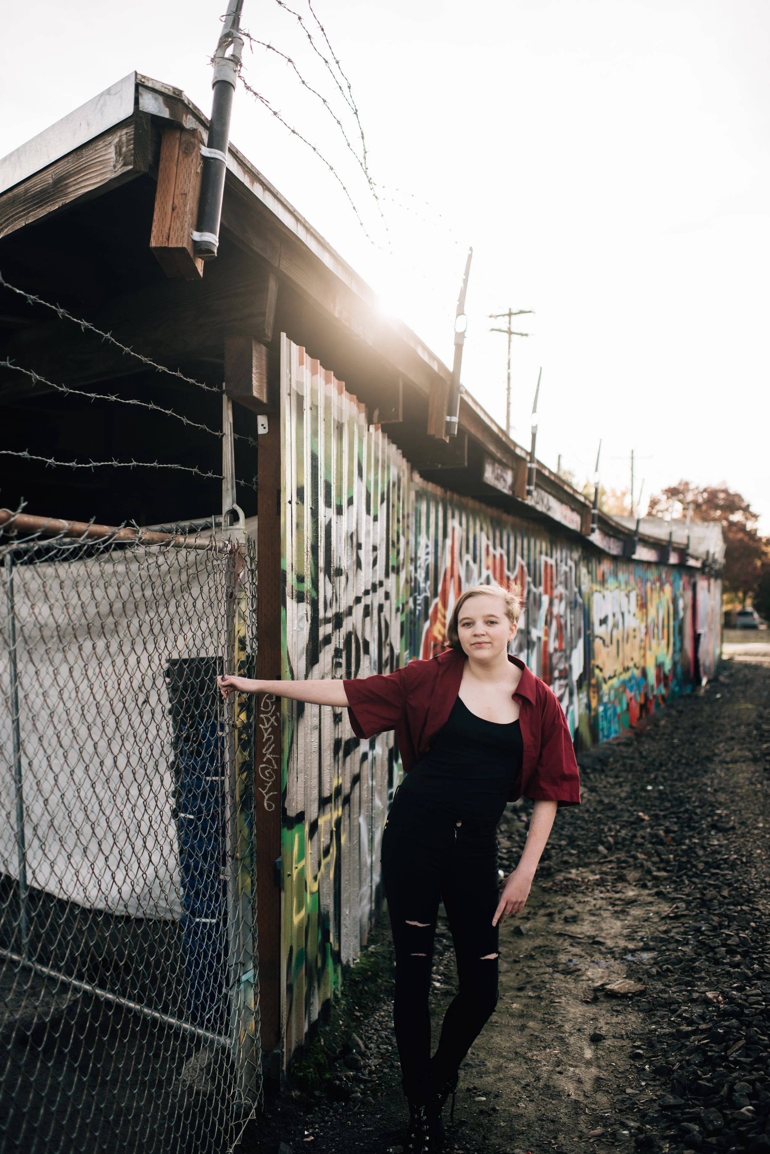 A high school senior holds onto a pole in front of a graffiti wall 