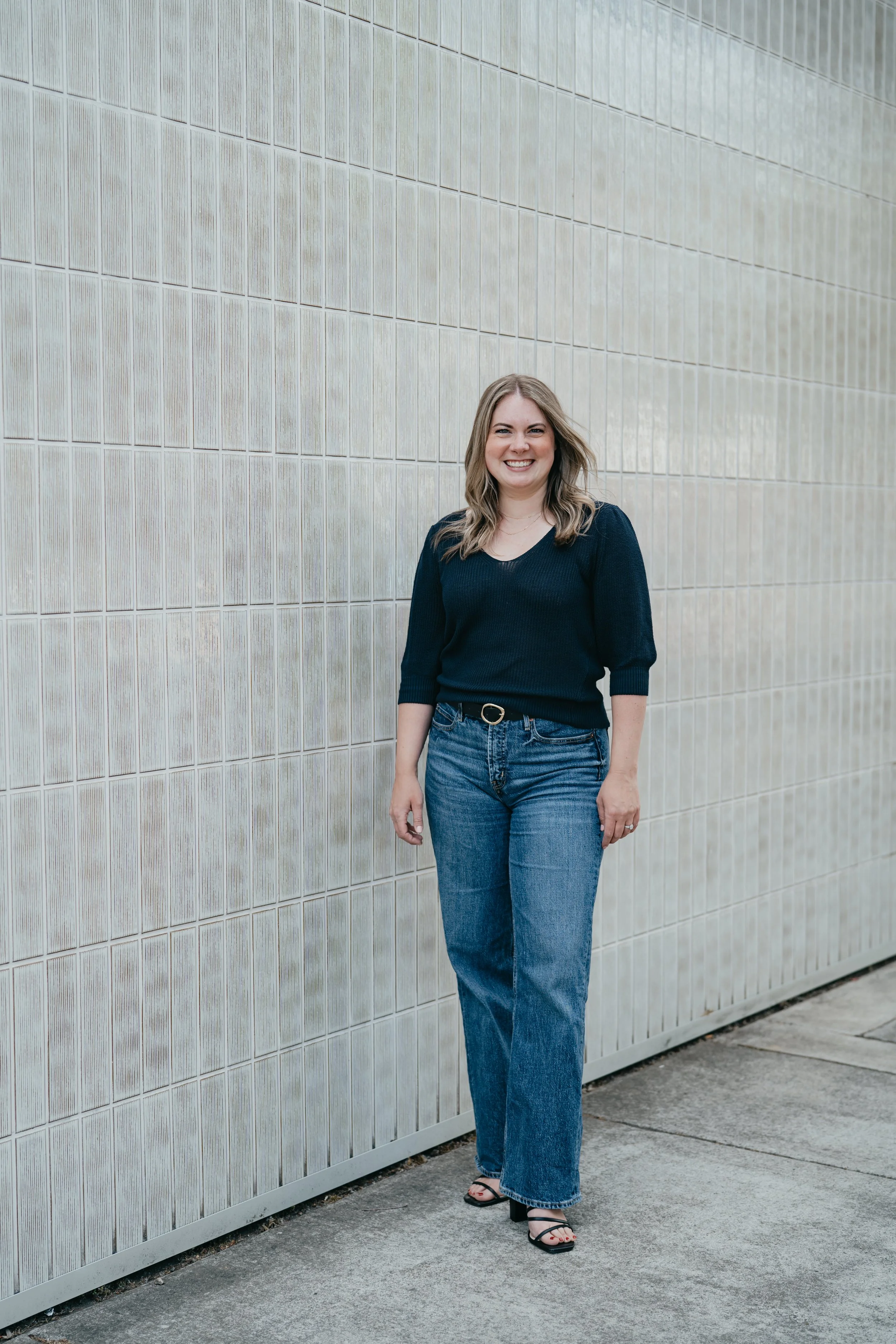 A confident female stands in front of a neutral back drop smiling at the camera
