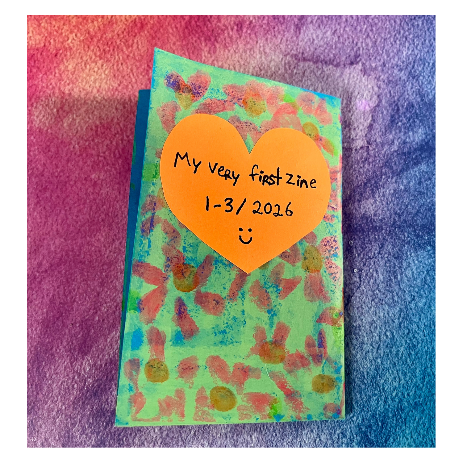 watercolor blue, purple, and pink gradient. Back cover of the zine with green and blue background and pink flowers. An orange heart reads: “My very first zine 1–3/2026 :).”