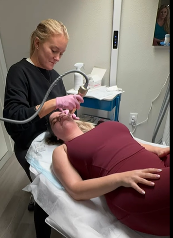 A woman receiving a facial treatment from a skincare professional in a clinic or spa setting.