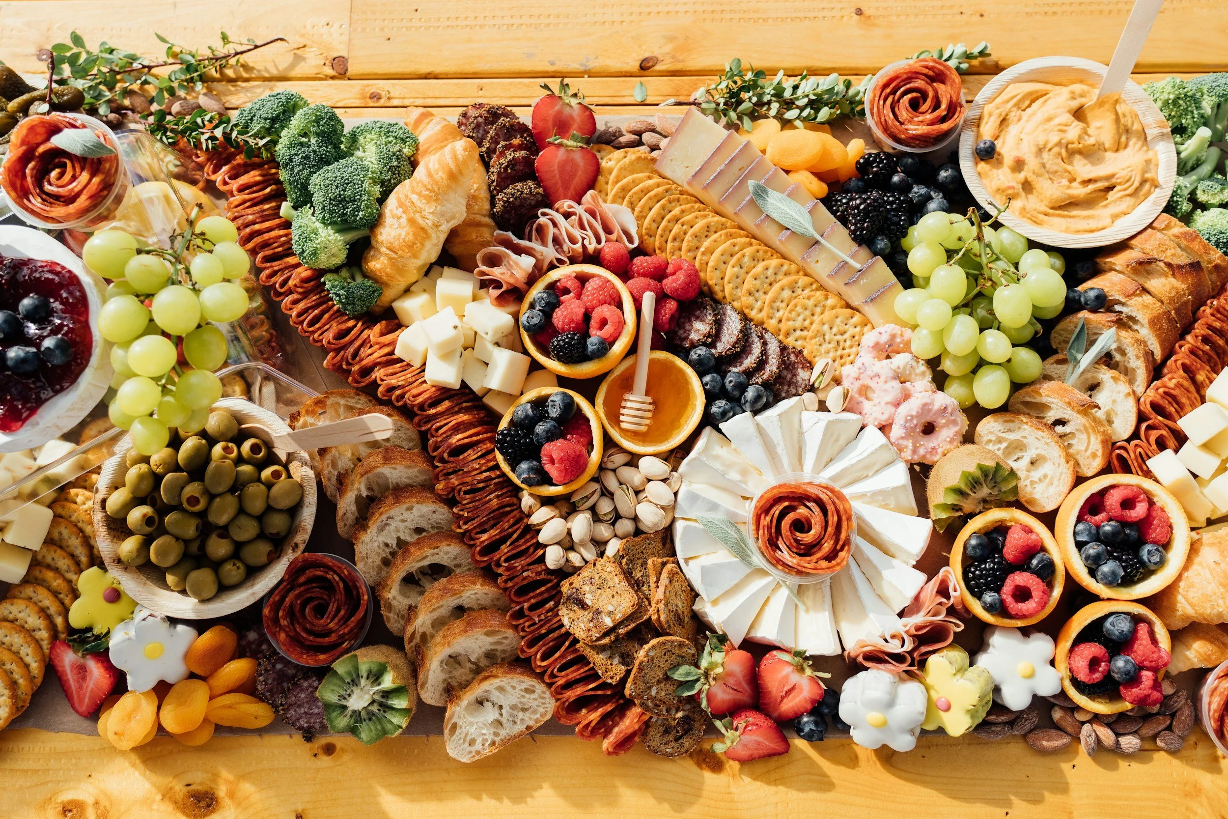 A colorful charcuterie board with cheeses, crackers, fruits, nuts, and spreads on a wooden surface.