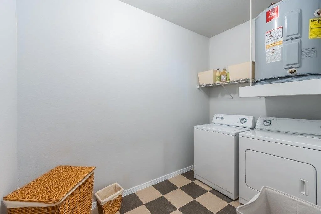 Laundry room with a washing machine, dryer, water heater, and shelf with cleaning supplies.