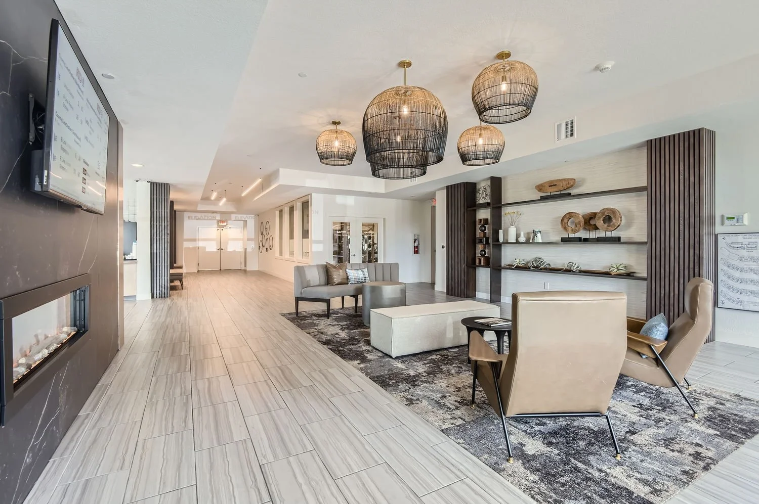 Modern hotel lobby with beige and brown furniture, decorative items on shelves, and large hanging light fixtures