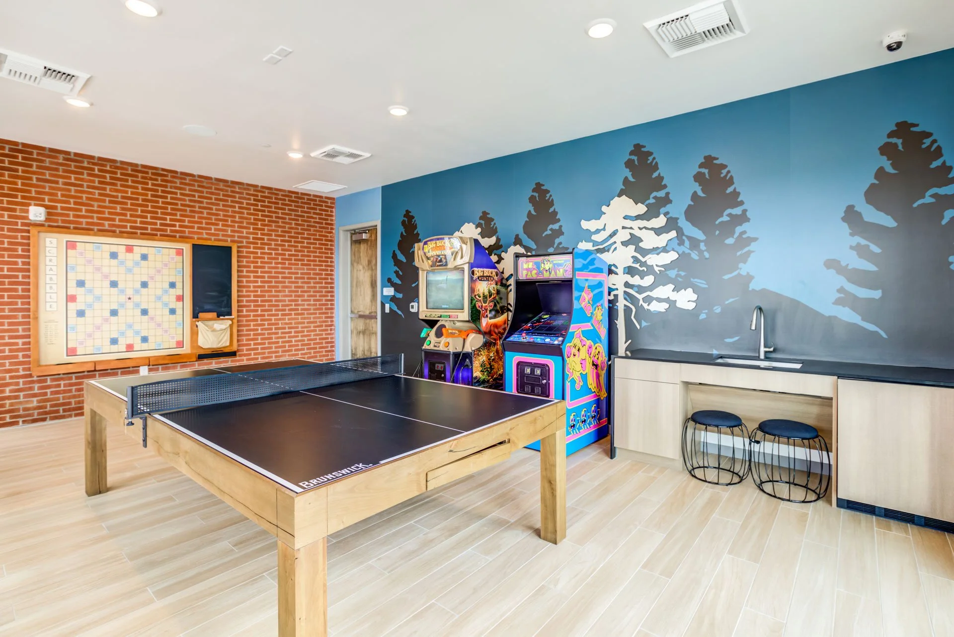 Indoor recreation room with a ping pong table, arcade games, a chalkboard, and a painted wall mural of pine trees.