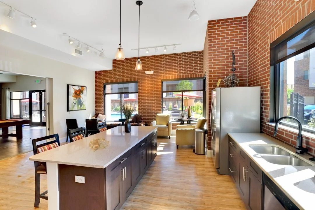 Open-concept kitchen and living area with brick walls, large windows, kitchen island with seating, and seating area with chairs and a sofa.