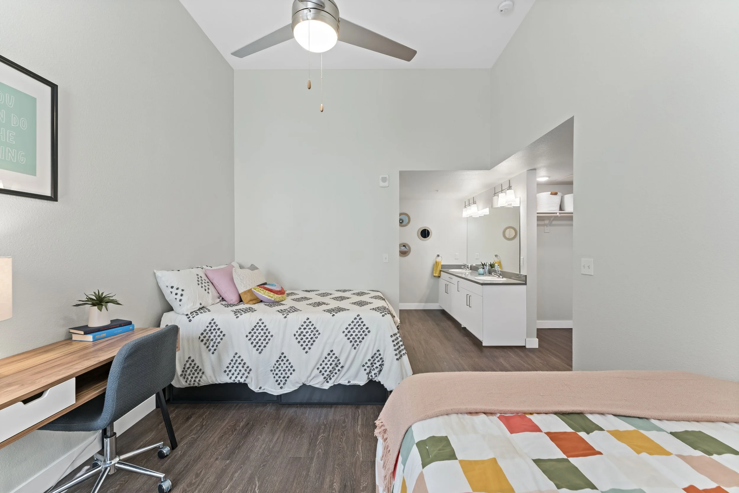 A bedroom with a bed, desk, and loveseat, open to a small kitchenette.
