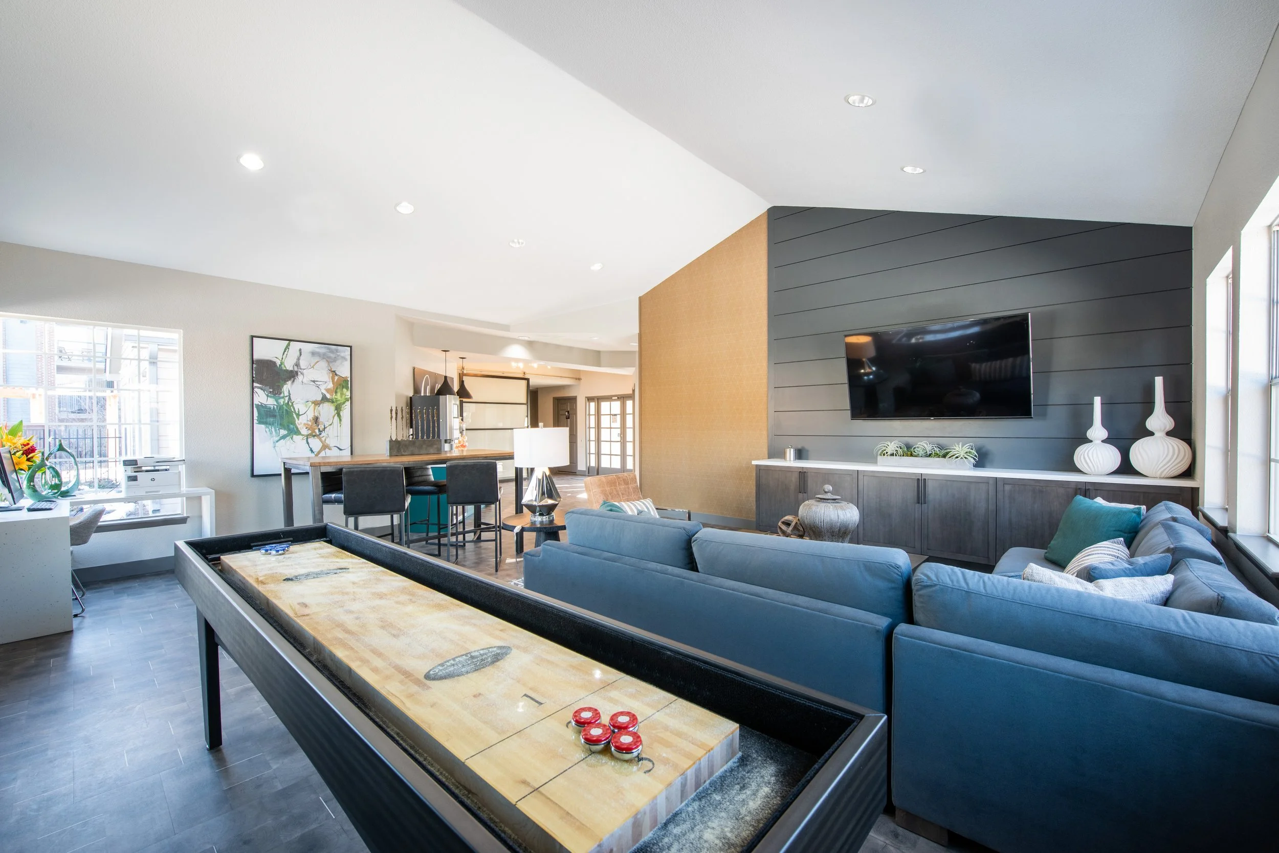 Modern living room with blue sectional sofa, wall-mounted TV, decorative vases, dining area, and large windows