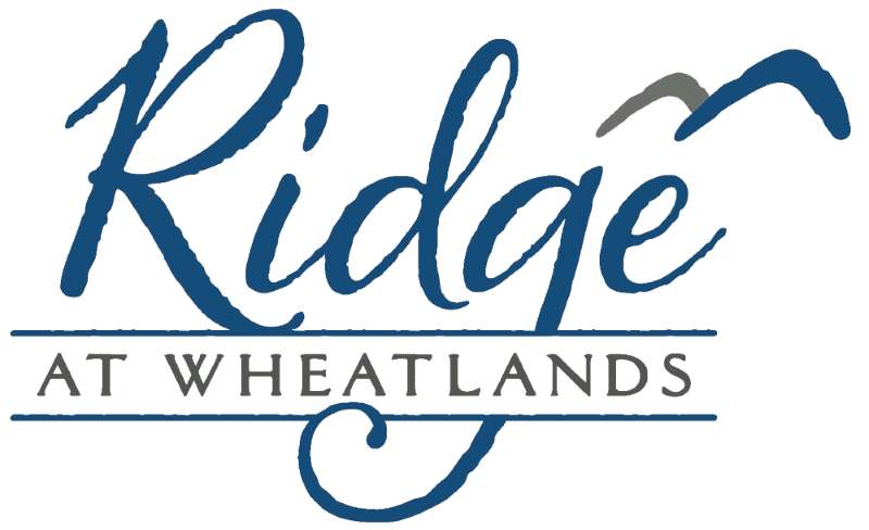 Logo for Ridge at Wheatlands, featuring the word 'Ridge' in large cursive blue font, and 'AT WHEATLANDS' in smaller capital gray letters underneath.