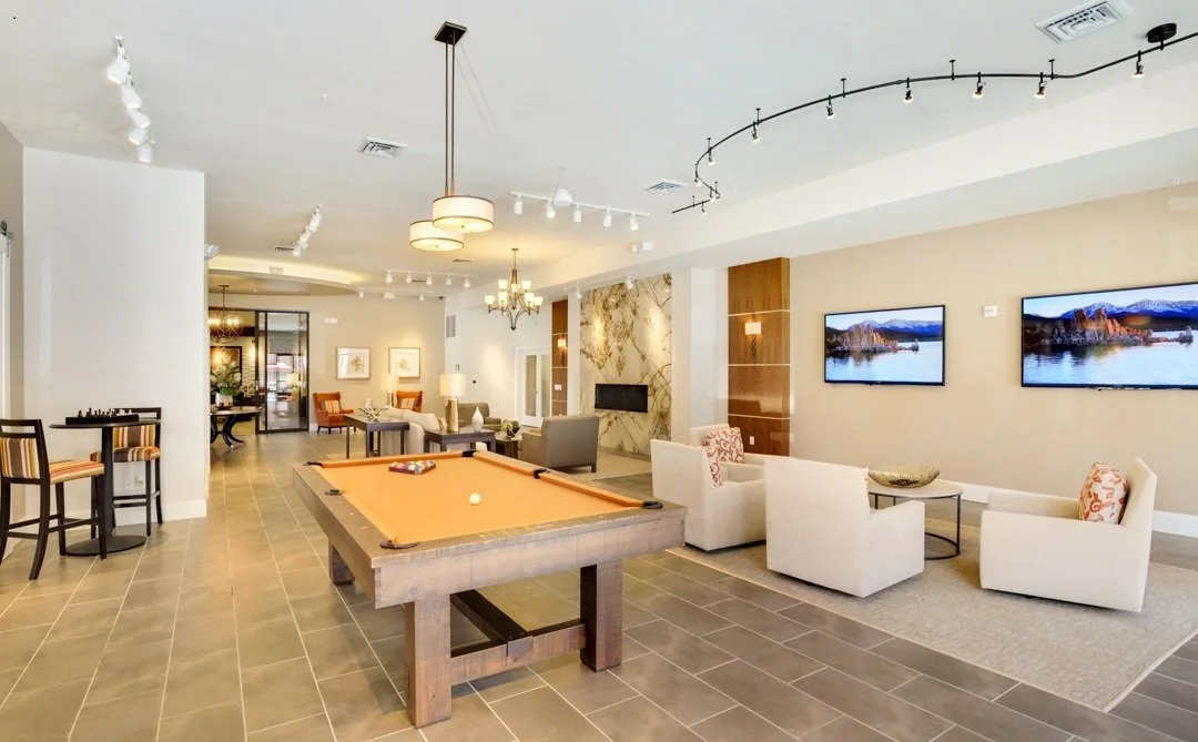 A spacious lounge with a pool table, multiple chairs and sofas, wall-mounted televisions, and a modern chandelier.