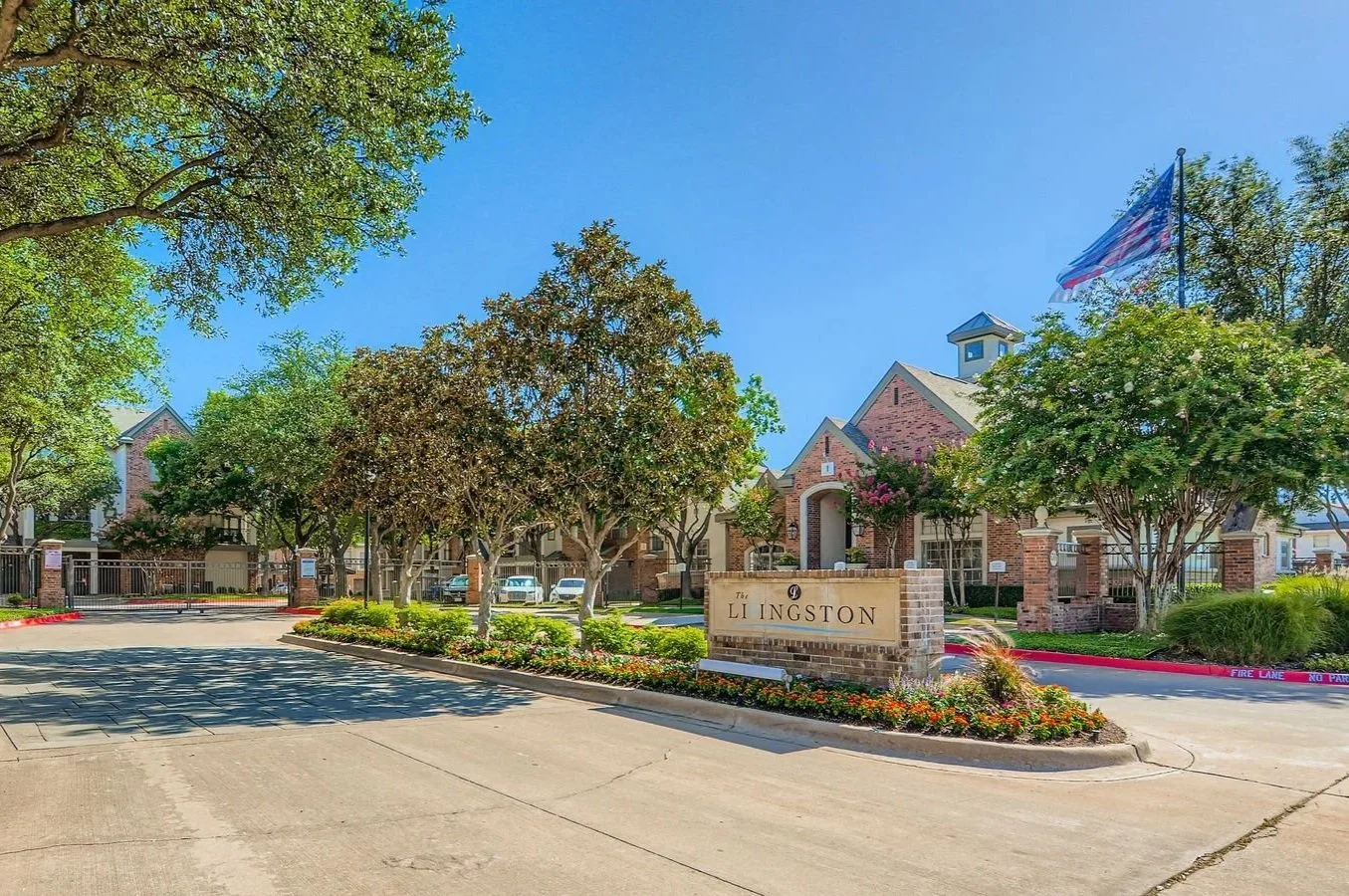Entry sign for The Lockington in a residential community with brick buildings, trees, and an American flag on a clear sunny day.