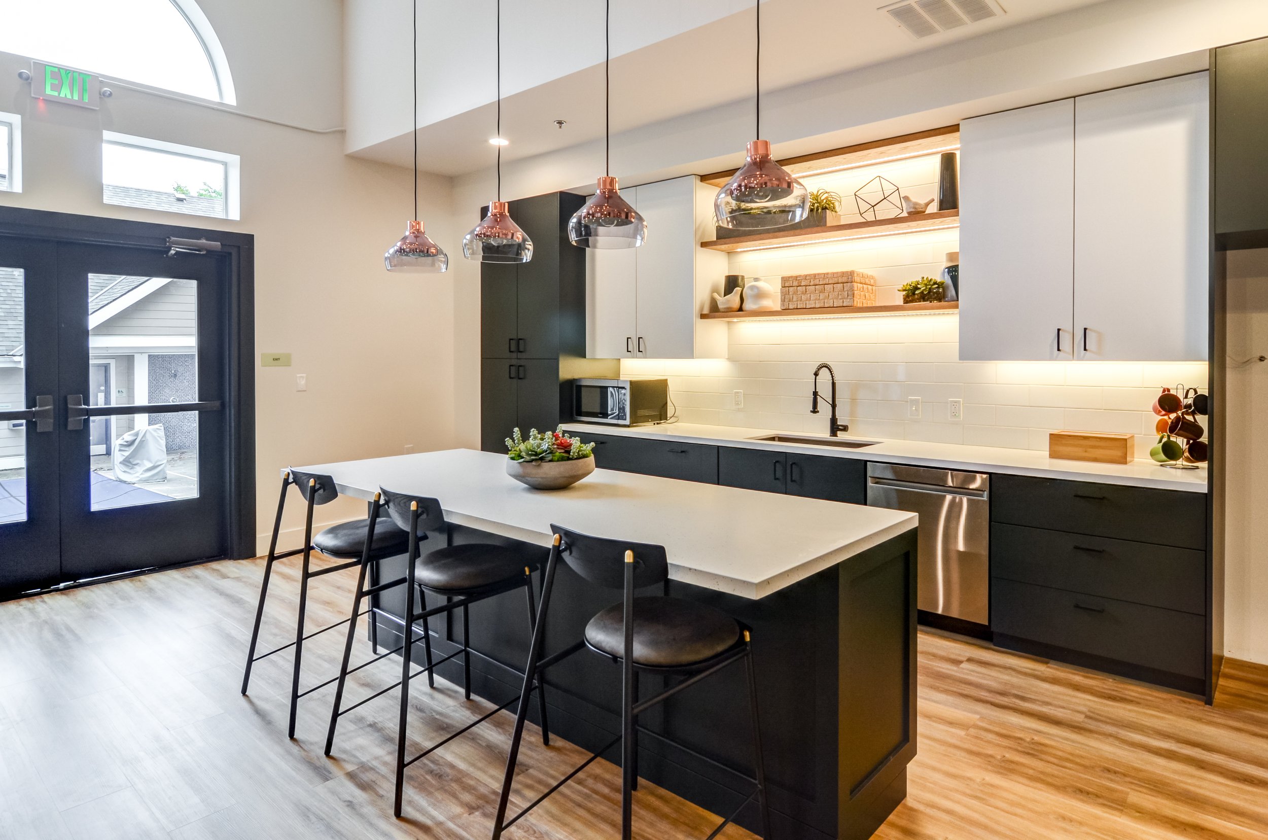 Modern kitchen with white and dark cabinetry, open shelves with decor, a large kitchen island with seating, pendant lights above, and a door leading outside.