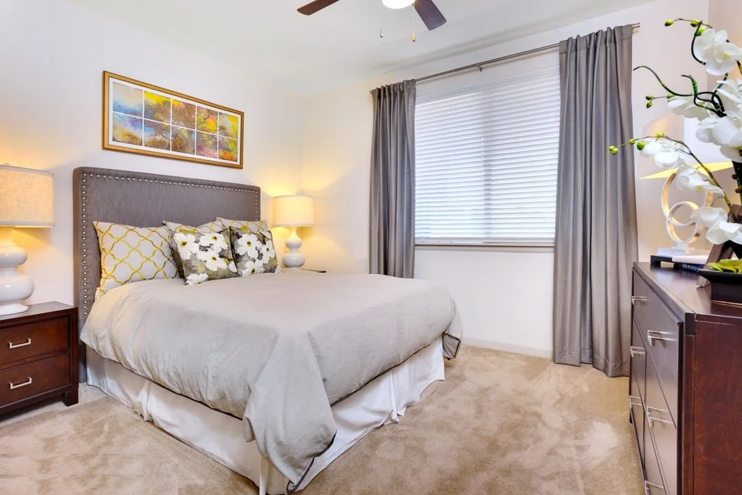 A bedroom with a bed, nightstands, lamps, a dresser, and curtains covering a window.