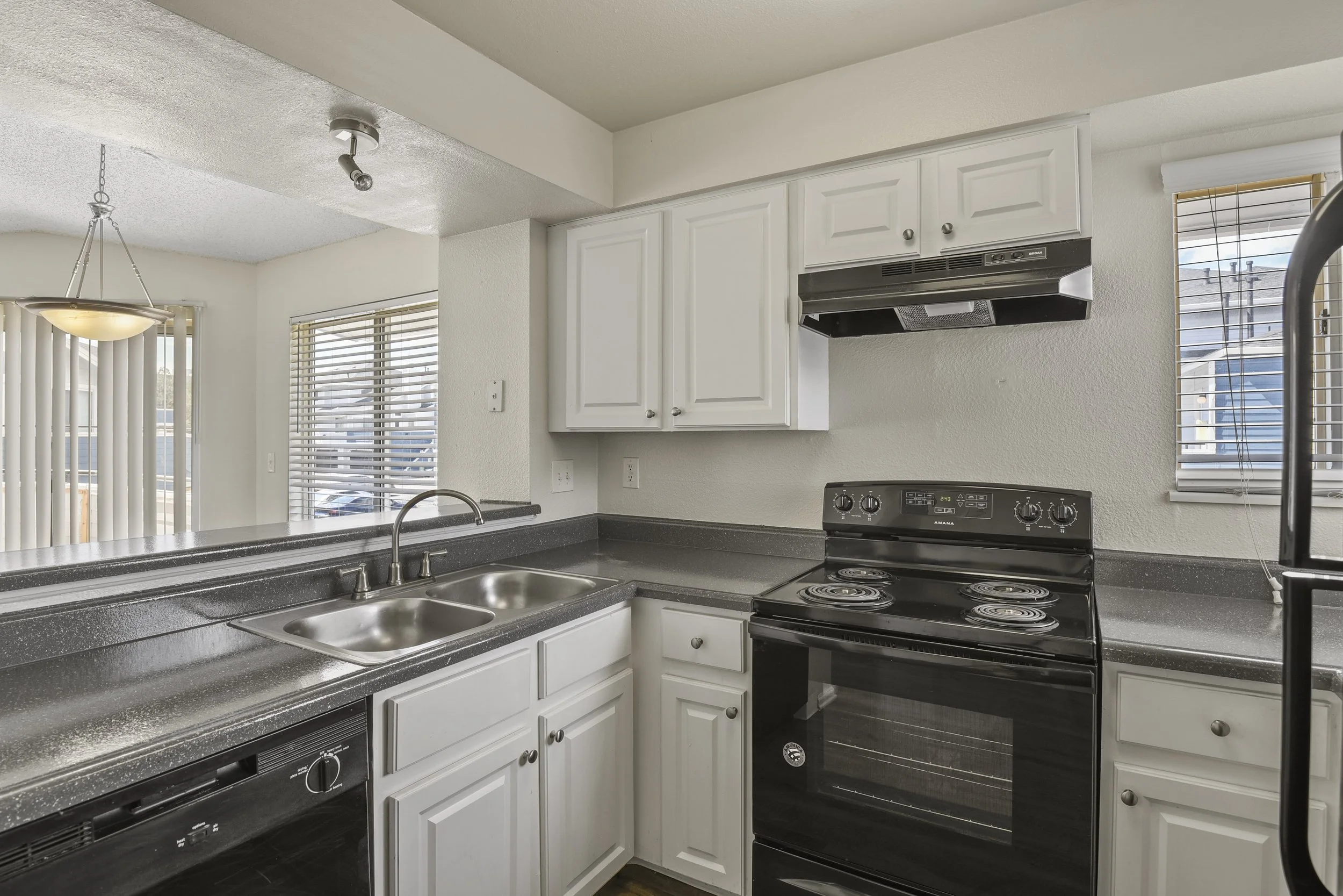 Kitchen with white cabinets, black stove, sink, and window with blinds.