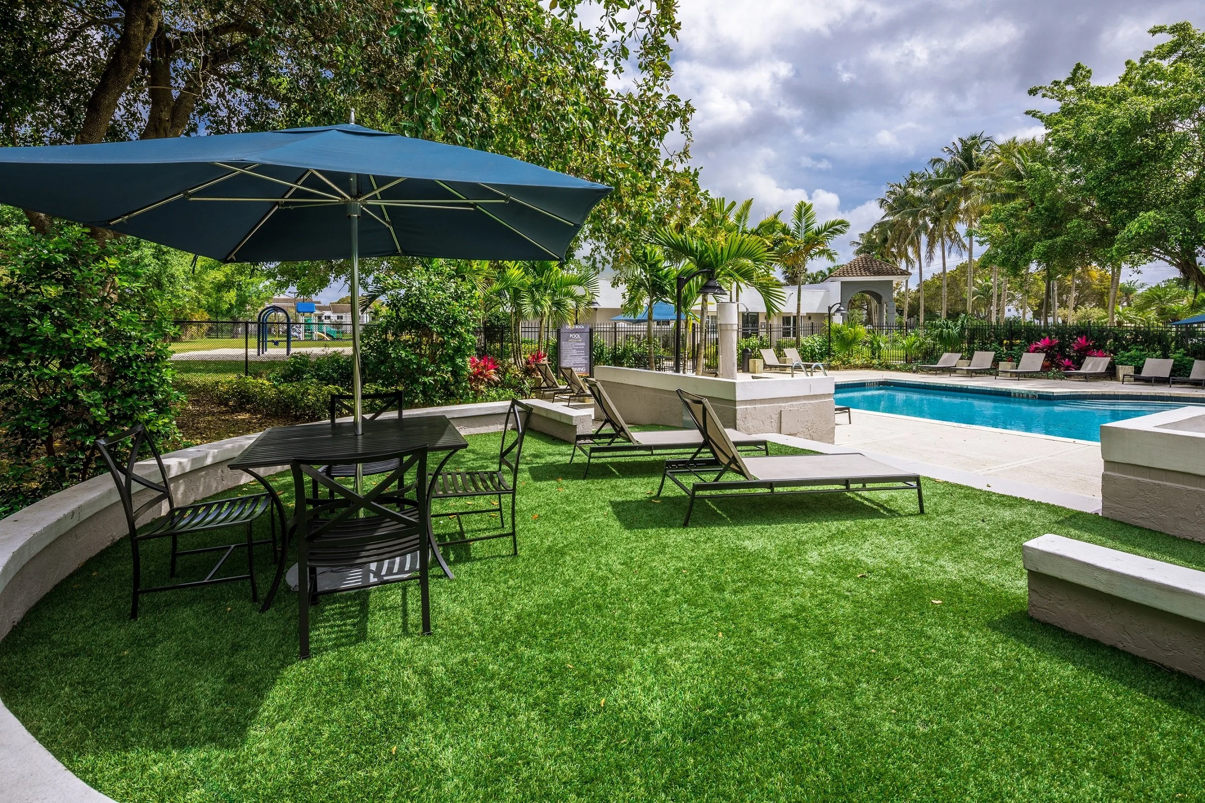 Pool area with lounge chairs, umbrellas, and surrounding lush green trees and plants during daytime.